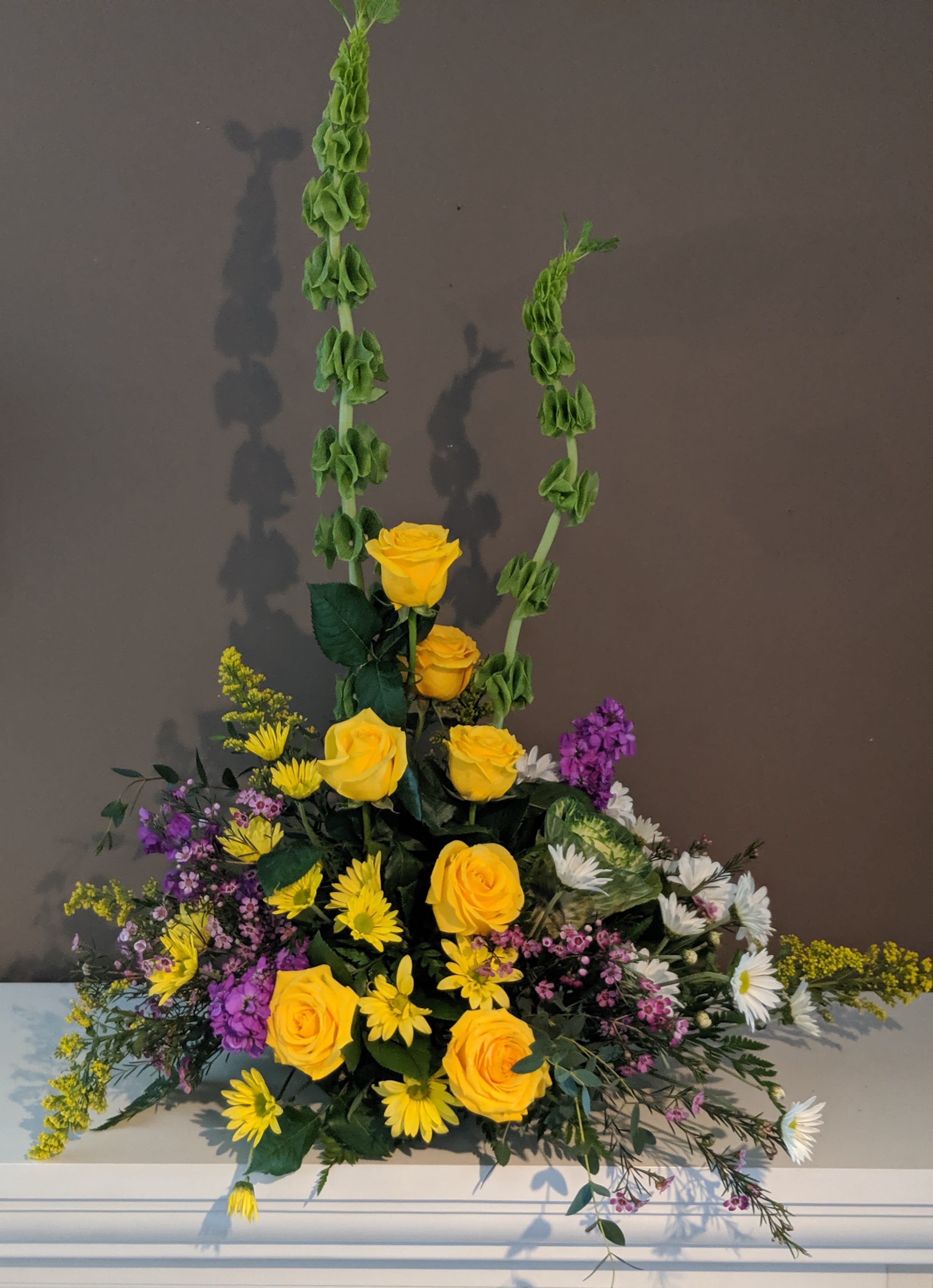 Tall floral arrangement with yellow roses, daisies, and purple accents