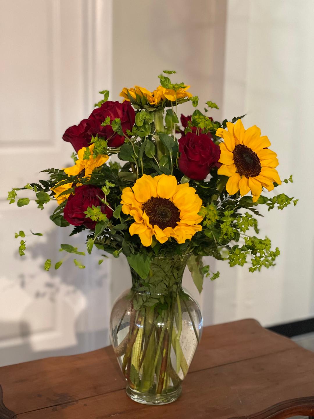 Red roses and yellow sunflowers arranged in a clear glass vase