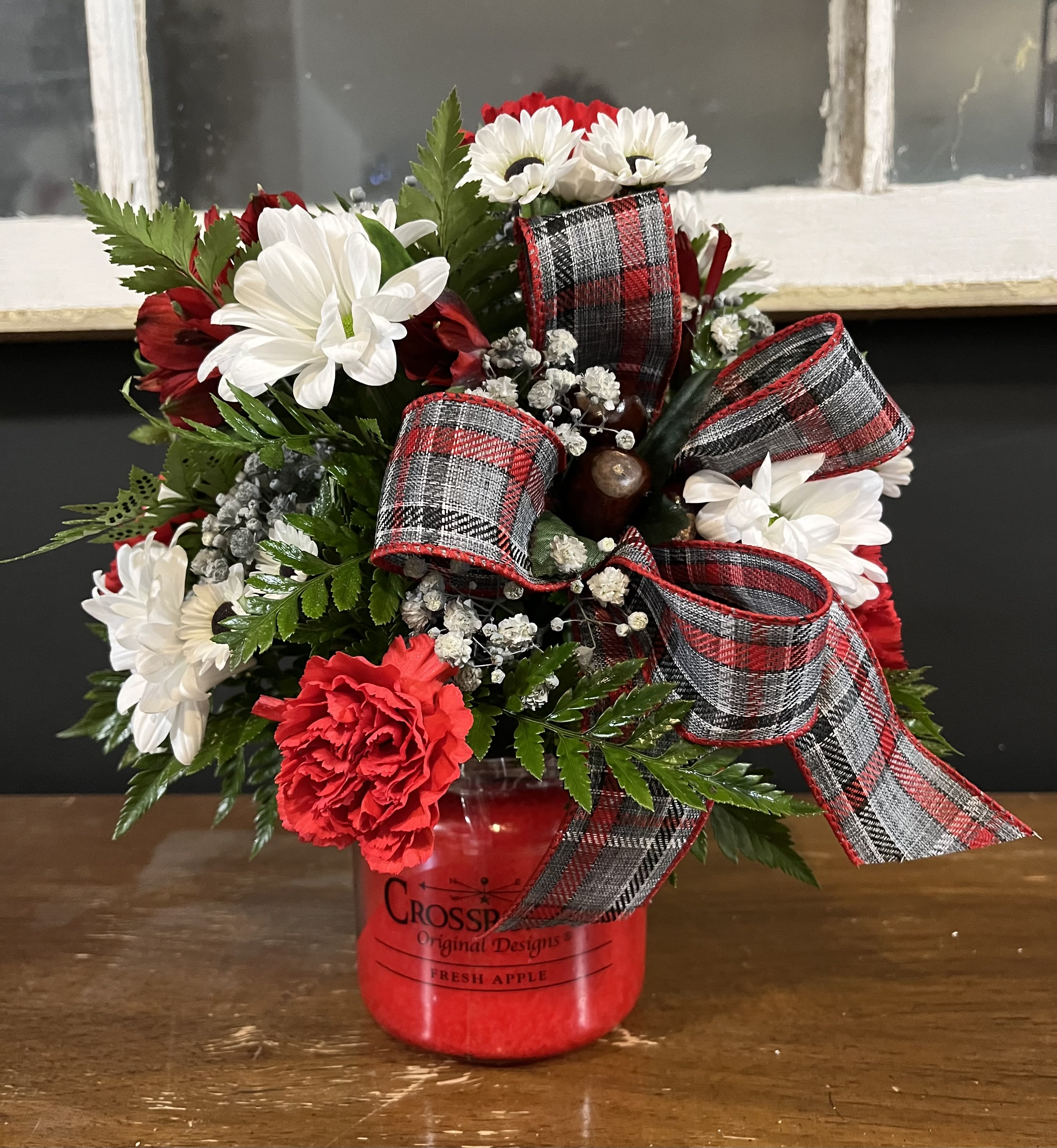 Red and white flower arrangement in a red jar with plaid ribbon