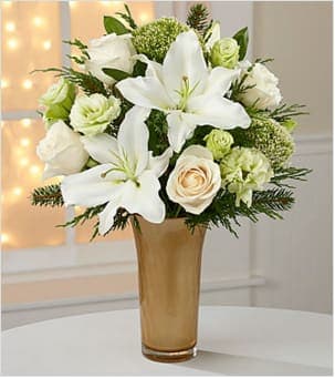 Holiday Glamour Rose &amp; Lily Bouquet - Picked fresh from the farm to send your warmest season's greetngs to friends and family near and far, the Holiday Glamour Bouquet shines with the light and beauty of the Christmas season. Hand gathered in select floral farms and blooming with the sophisticated sweetness of winter whites, this fresh flower arrangement has been picked fresh for you to help you celebrate with a modern styling that glows with the love and generosity of the holiday season. This bouquet includes: white Oriental Lilies, cream roses, white double lisianthus, white trachelium, and an assortment of lush holiday greens. Presented in a designer optic trumpet vase in a golden hue.  BETTER bouquet includes 12 stems. Approximately 17"H x 16"W. Your purchase includes a complimentary personalized gift message.