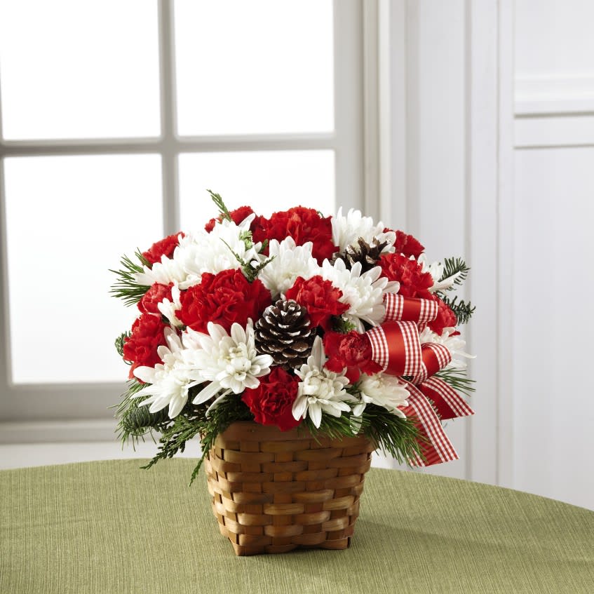The FTD Holiday Happiness Basket - Merry and bright, this joyful holiday bouquet is ready to spread Christmas greetings with each beautiful bloom. Red roses, red carnations, and red mini carnations are highlighted by snowy white chrysanthemums, white-tipped pinecones, and lush greens, accented with a red country check ribbon while seated in a dark stained woven woodchip basket. A Christmas flower arrangement that speaks to the happiness and treasured moments that this special time of year holds! 