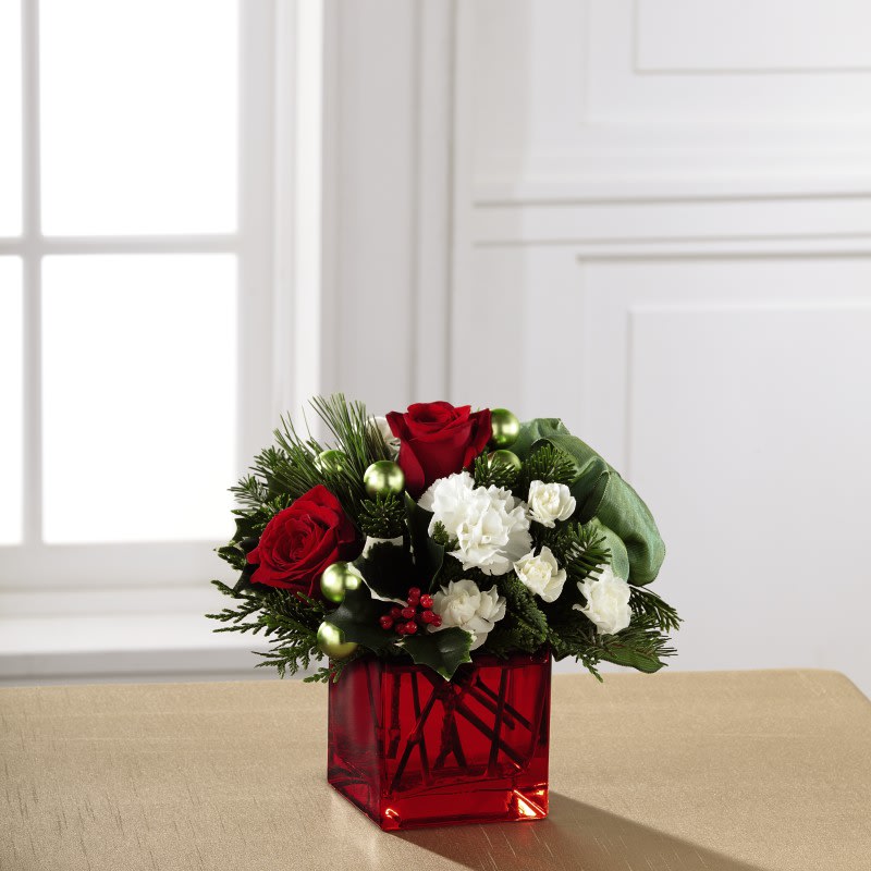 The FTD¨ Merry &amp; Brightª Bouquet - Blossoming with a Christmas charm that evokes memories of holiday seasons long past while nodding towards a sophisticated modern styling, this holiday flower arrangement is ready to spread the joy of the season to your recipient. Rich red roses and white carnations and mini carnations are artistically arranged amongst variegated holly and an assortment of fresh Christmas greens. Accented by matte green glass holiday balls and a sage green wired taffeta ribbon while seated in a red glass cubed vase, this stunning Christmas flower bouquet is ready to create a holiday memory your recipient will never forget. 