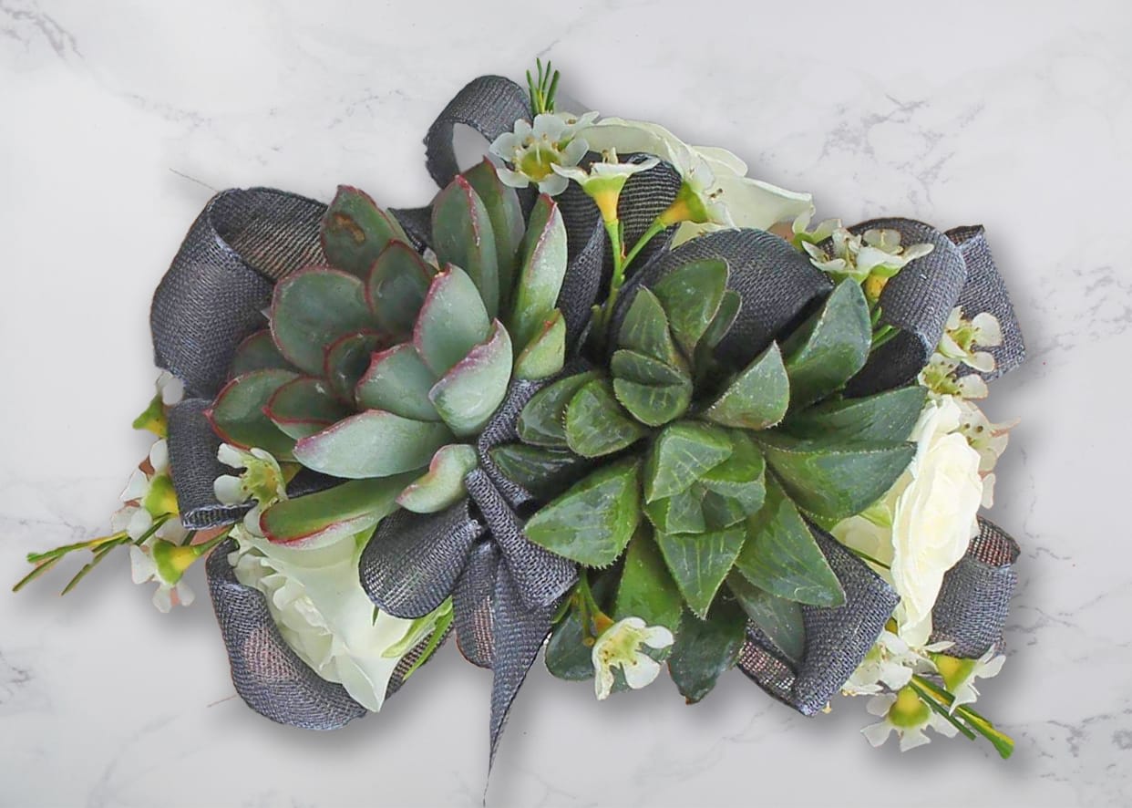 Succulent arrangement with white flowers and dark ribbon on a light surface