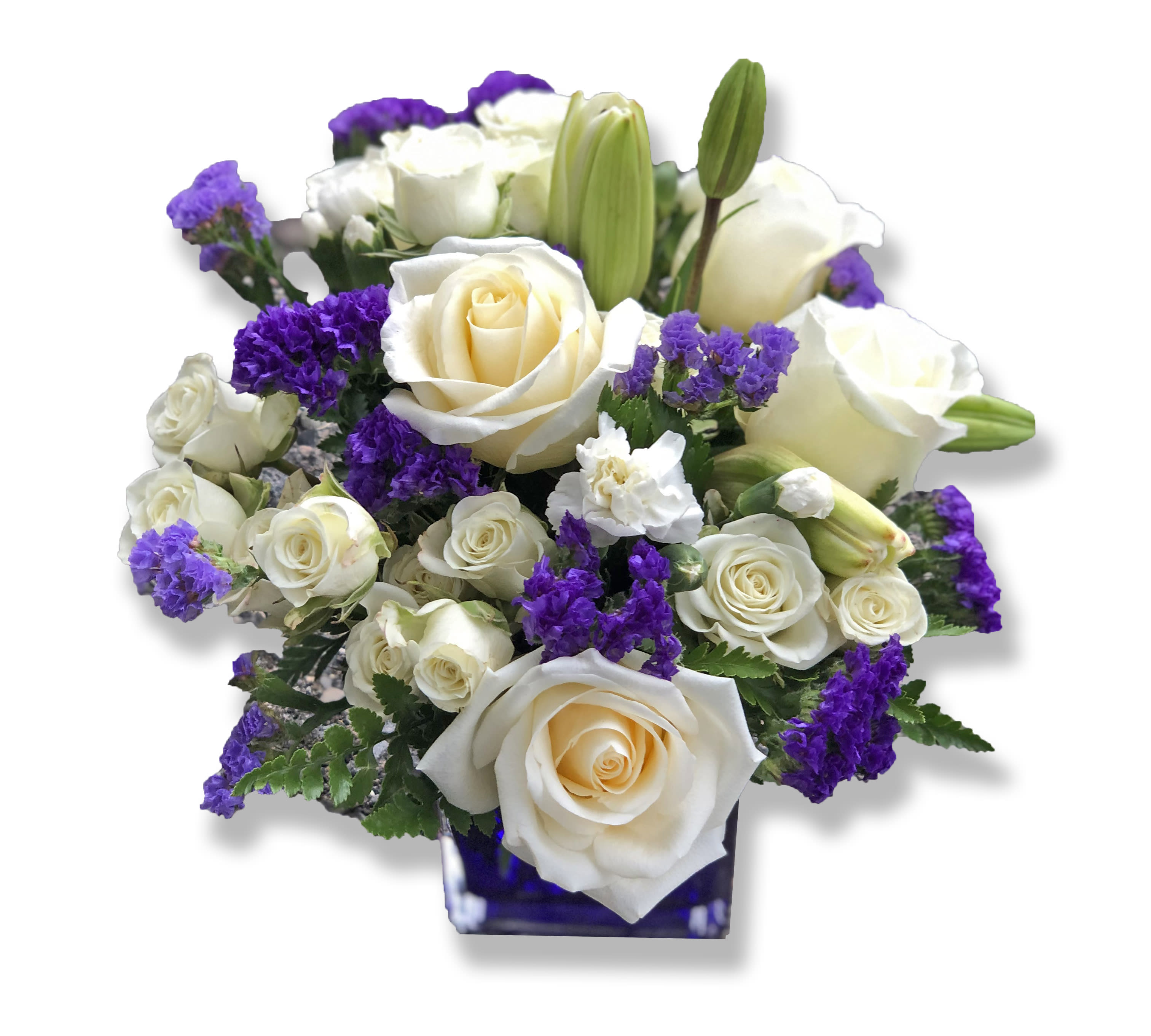 Teleflora's Sapphire Skies Bouquet - Send someone a bit of heaven with this beautiful bouquet. Luxurious crème roses and pure white lilies paint a peaceful picture inside a sapphire blue cube.  Crème roses, white asiatic lilies and white miniature carnations are mixed with bursts of purple statice and green pitta negra. Delivered in a glass Cube.  Approximately 12" W x 11 1/2" H  Orientation: All-Around  As Shown : TEV25-3A Deluxe : TEV25-3B Premium : TEV25-3C 