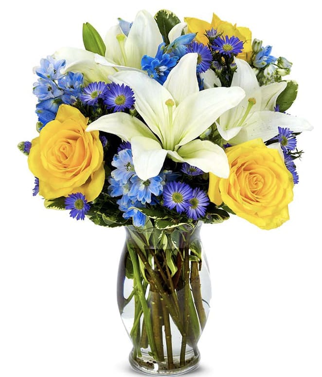 Bouquet of white lilies, yellow roses, and blue-purple flowers in a glass vase
