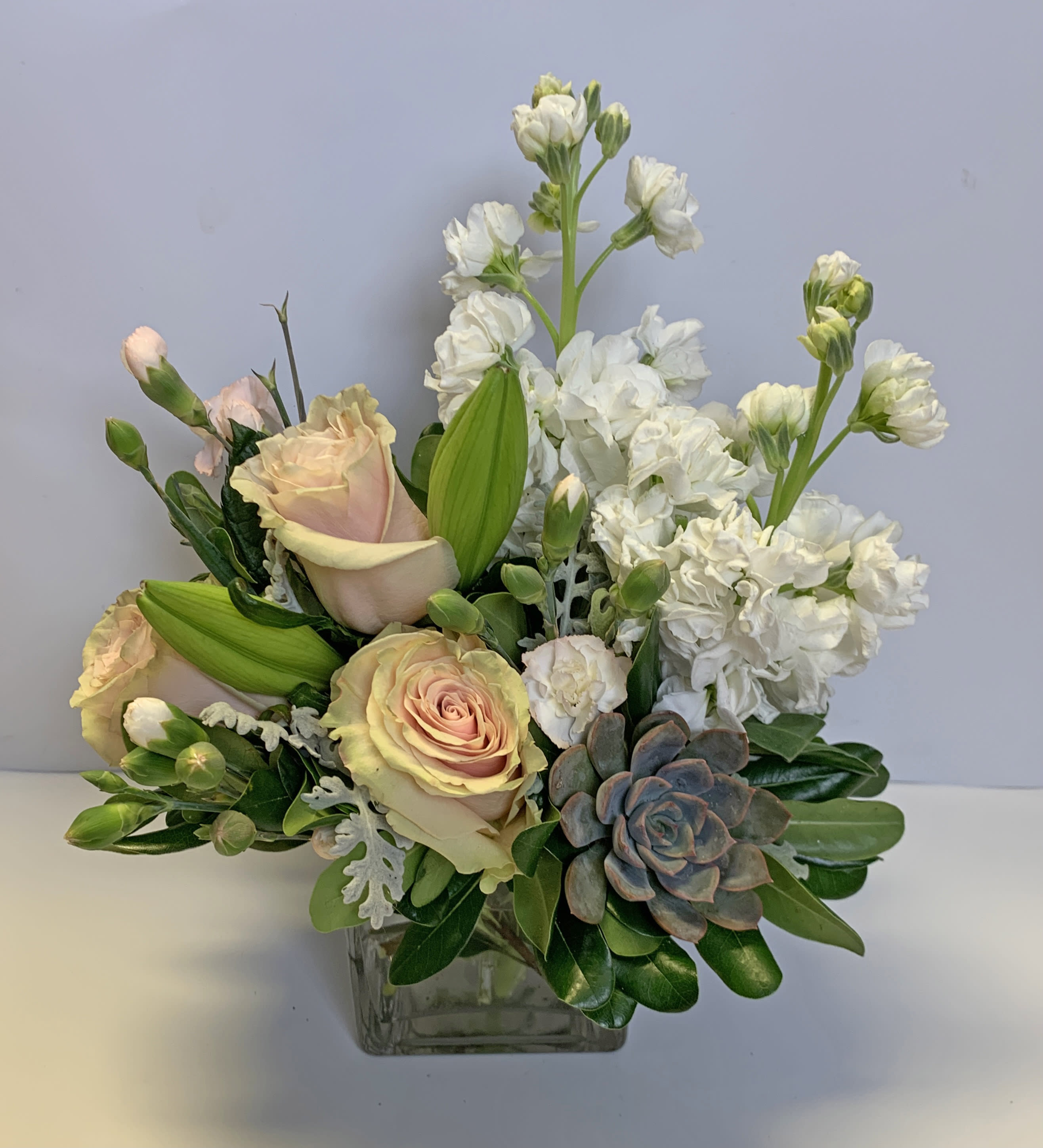 Pastel roses and white blooms arranged in a square glass vase