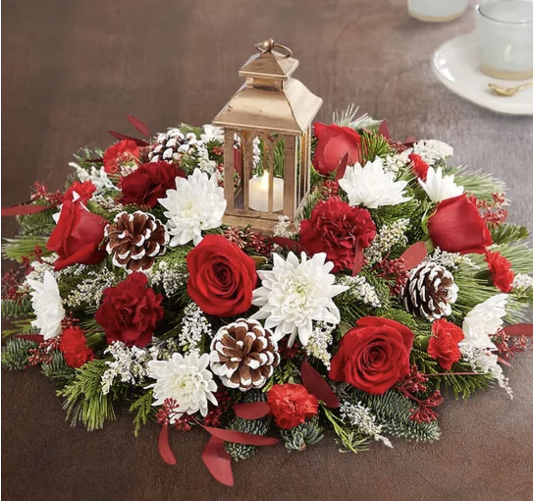 Round floral centerpiece with red roses, white mums, pinecones, and a lantern