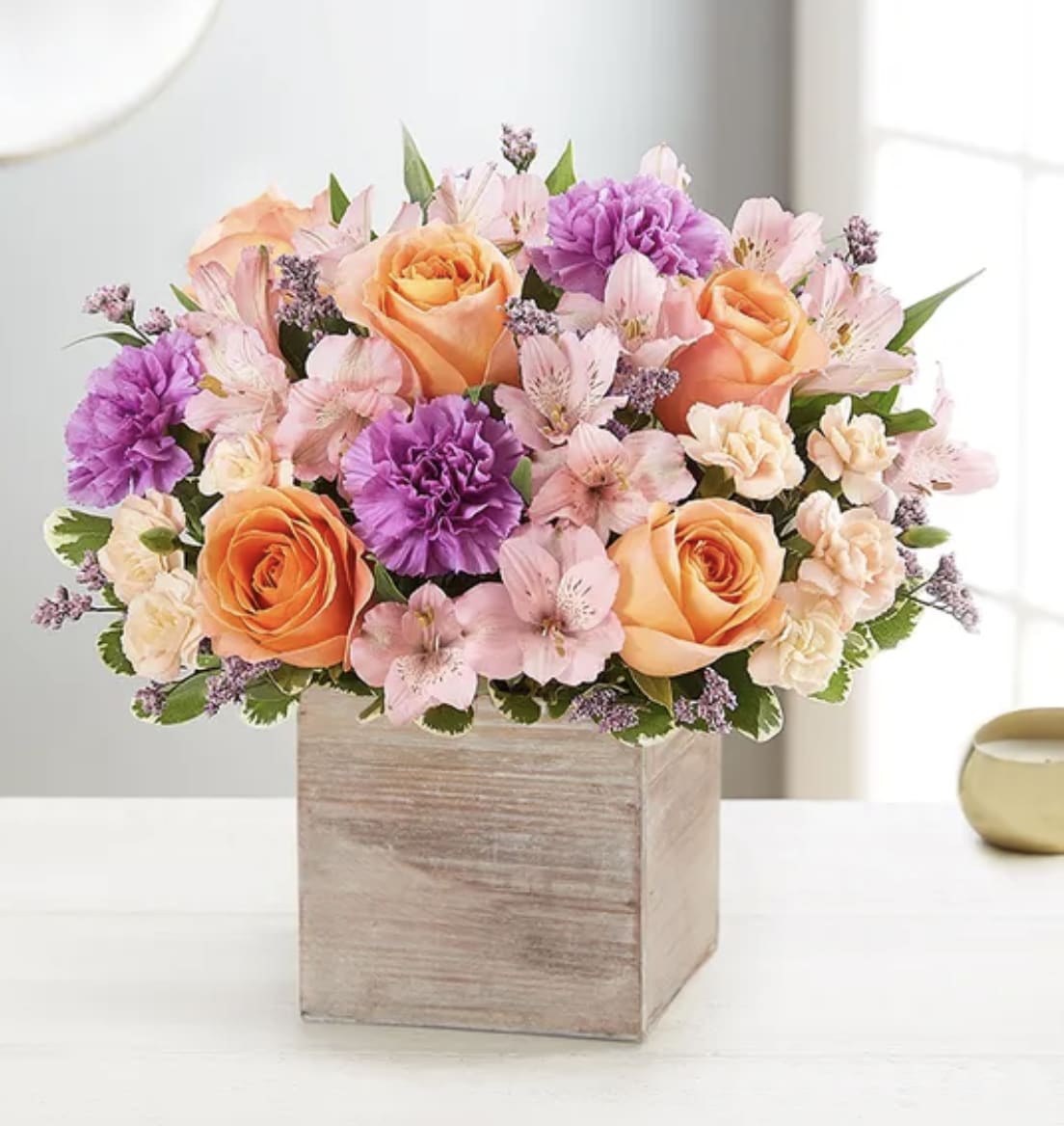 Bouquet of peach roses, pink flowers, and purple carnations in a wooden box