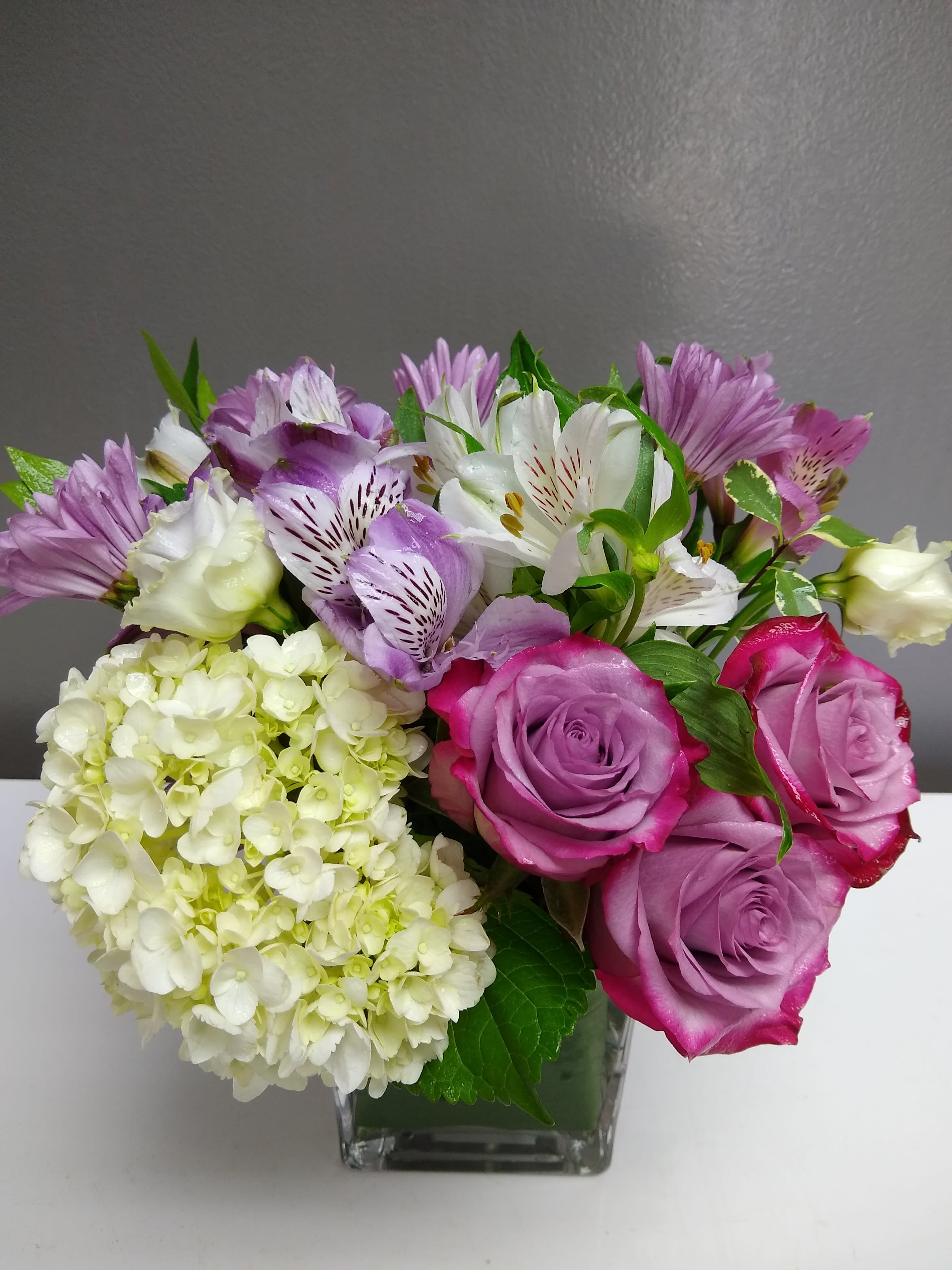 Bouquet of purple roses, white lilies, and pale hydrangea in a glass vase
