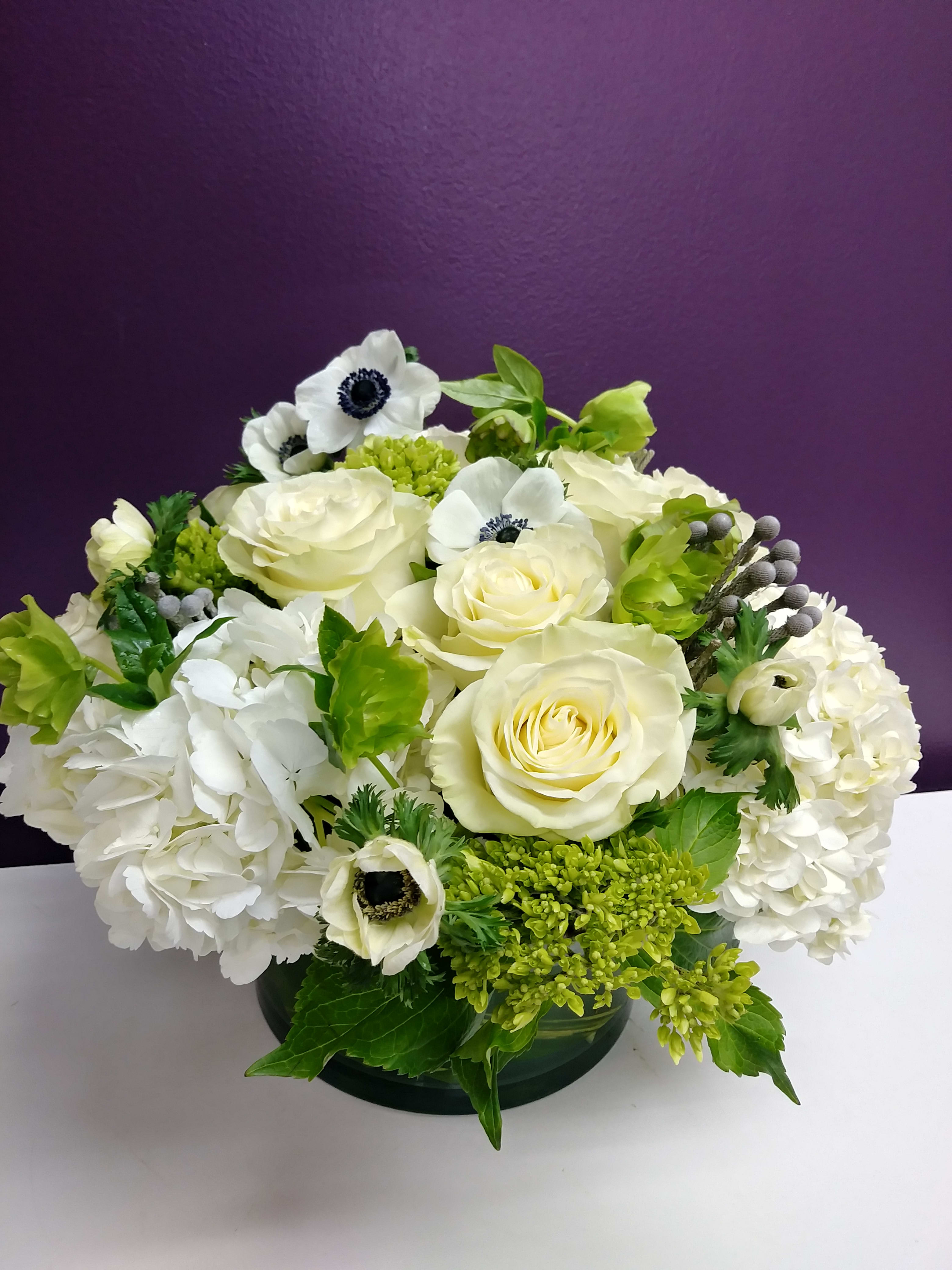 White roses and hydrangeas with green accents in a low vase arrangement