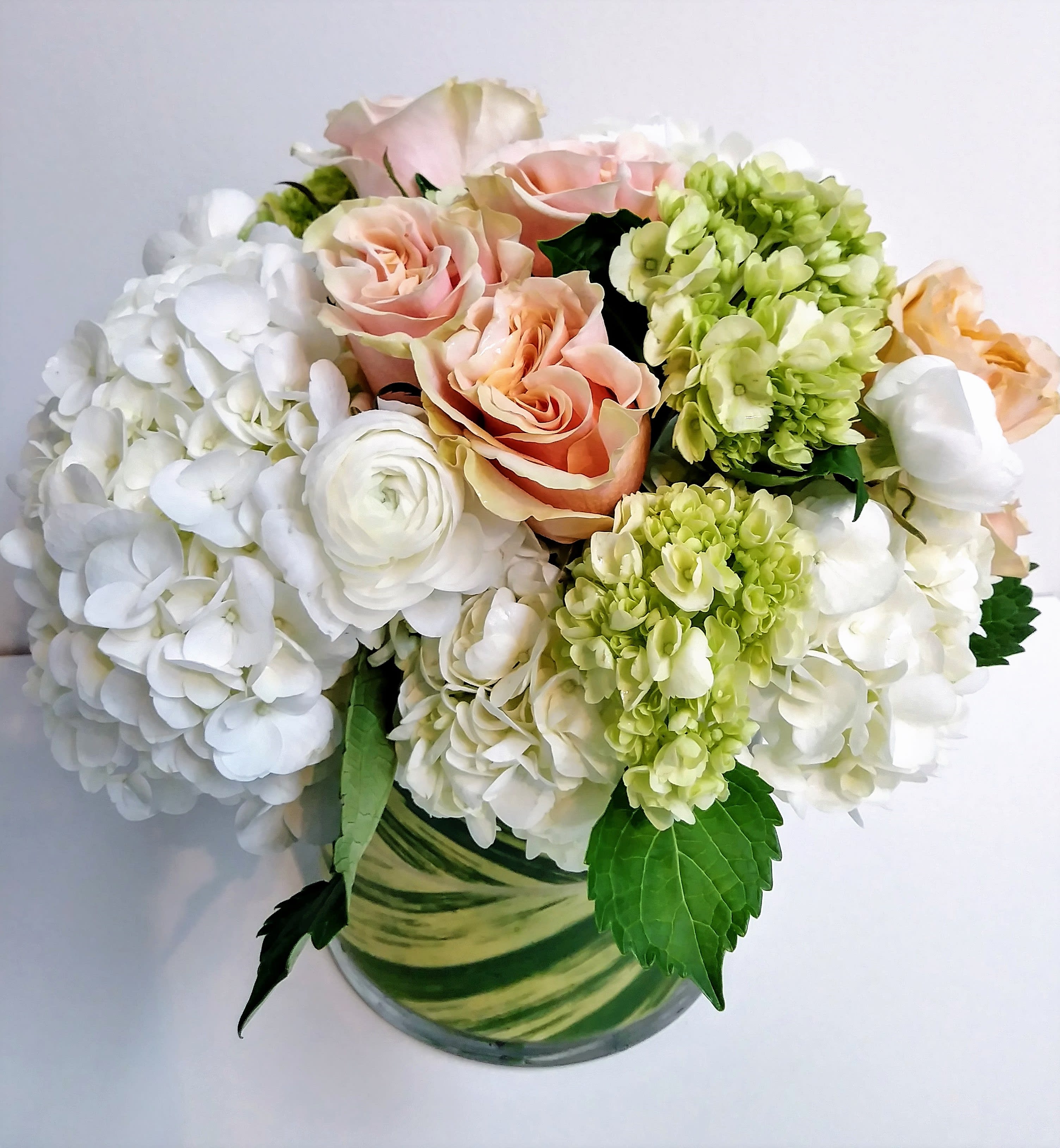 Bouquet of white hydrangeas, peach roses, and green blooms in a glass vase