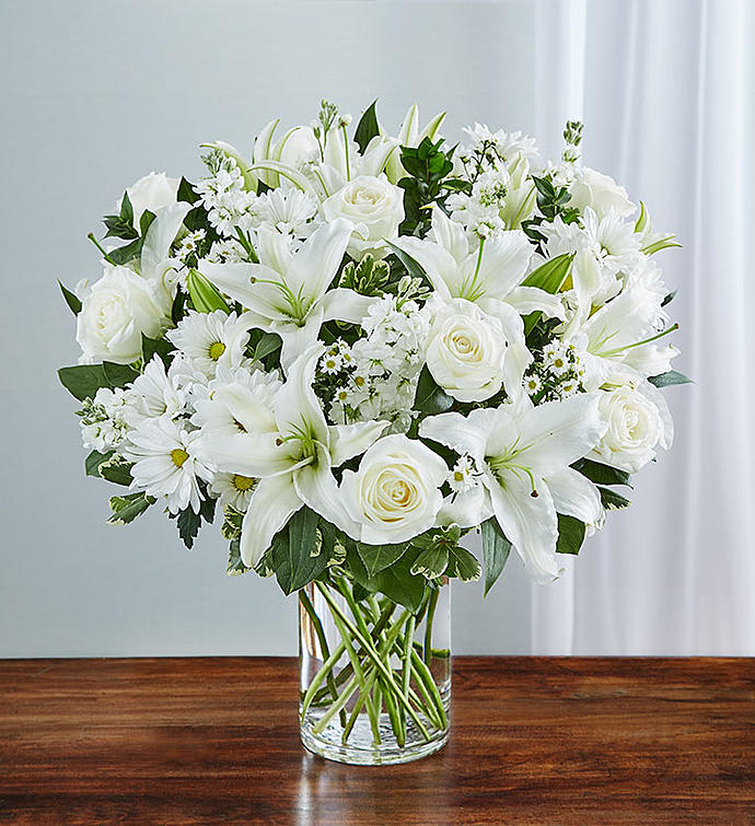 White lilies, roses, and daisies arranged in a clear glass vase