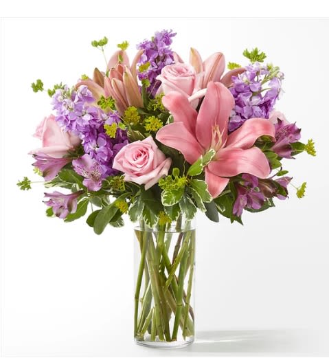 Pink lilies and roses in a clear glass vase with purple flowers
