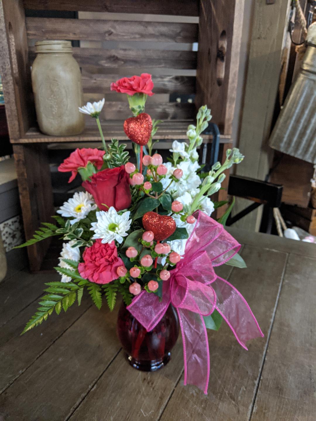 Pink and white floral arrangement in a red glass vase with a pink bow