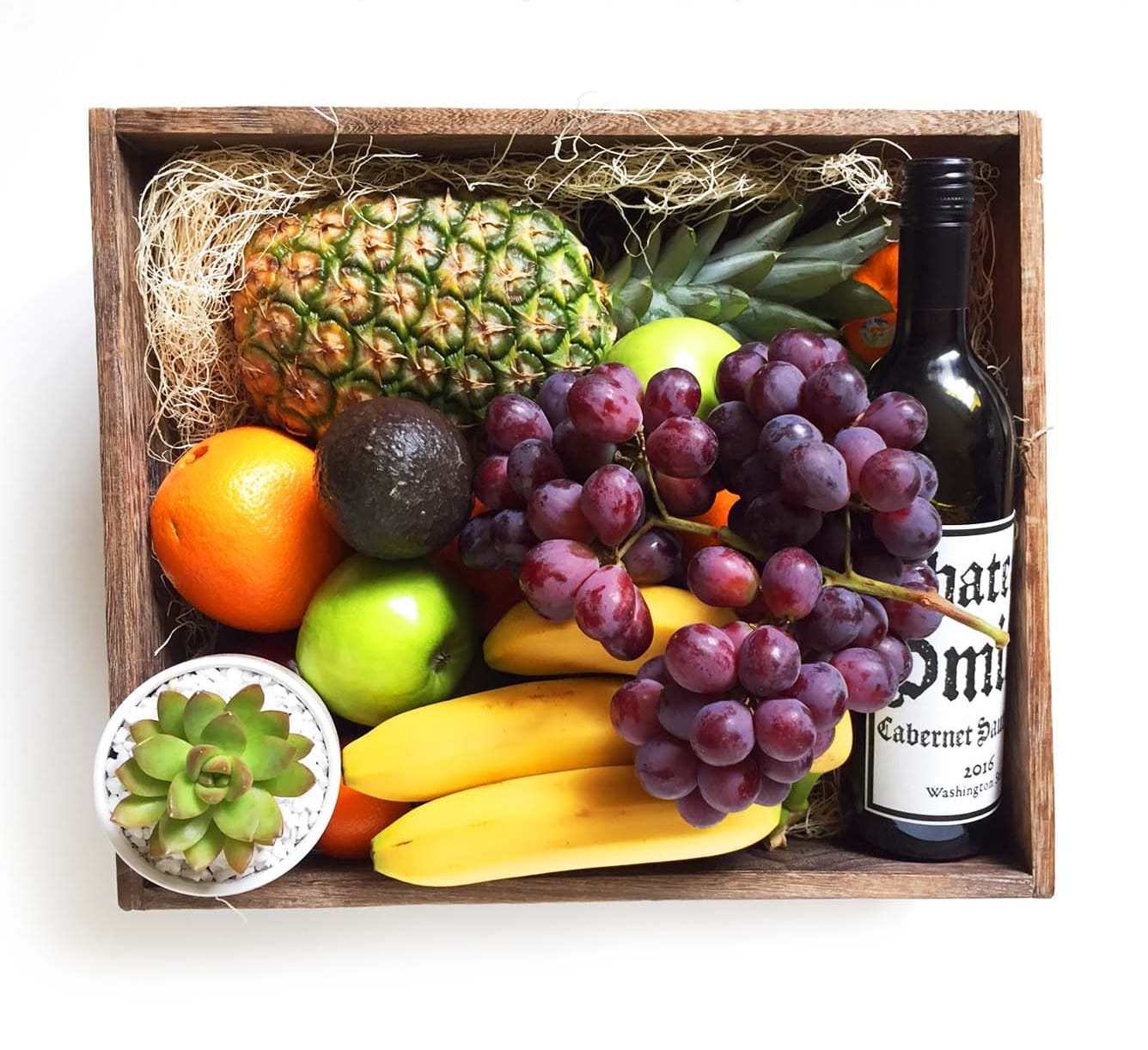 Fruit gift box with grapes, pineapple, bananas, citrus, avocado, and a wine bottle