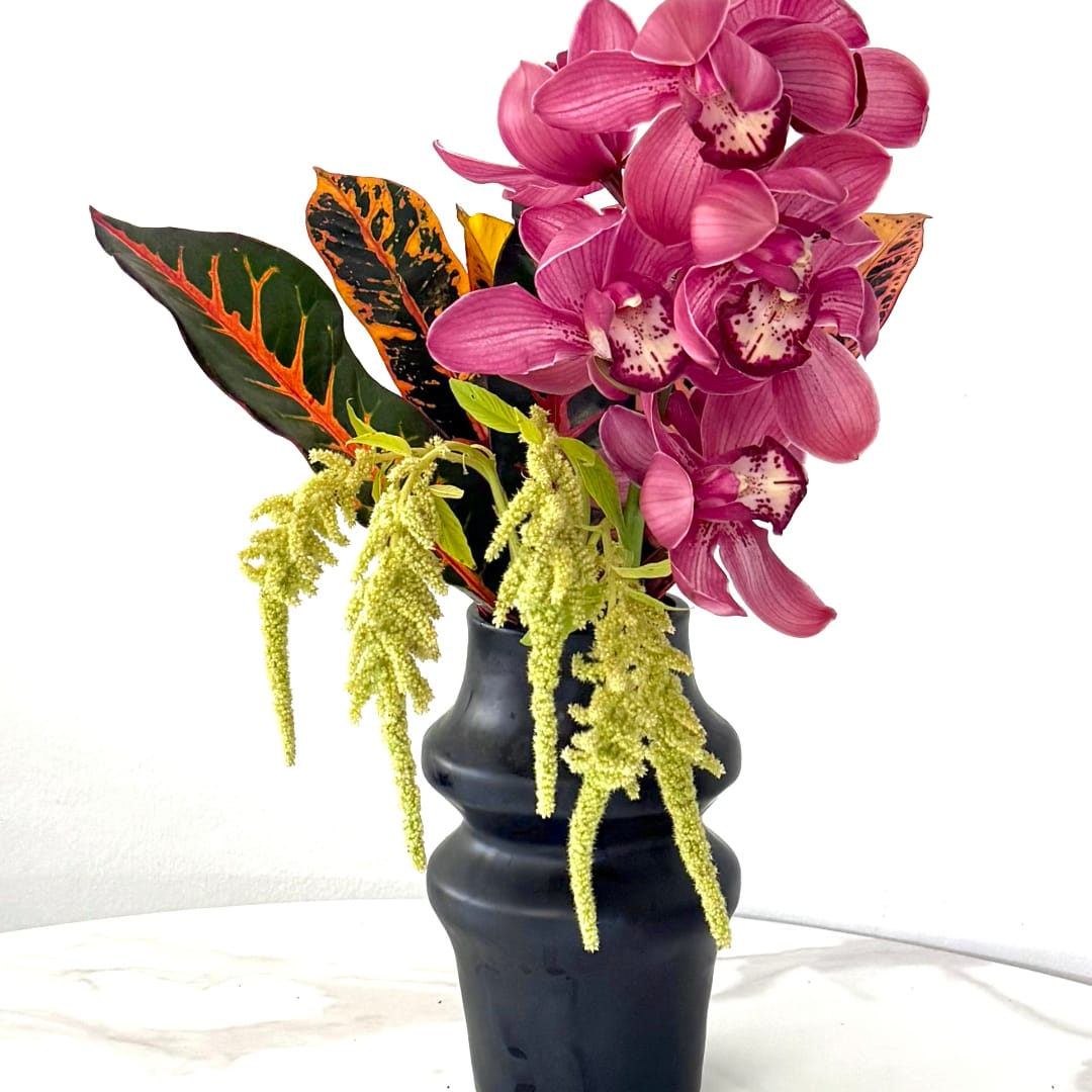 Pink orchids in a black vase with variegated leaves and hanging yellow blooms