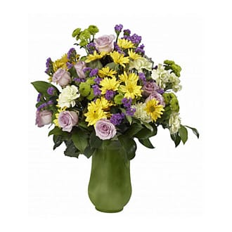 Mixed bouquet of yellow, purple, and pale pink flowers in a green vase
