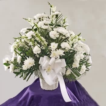 Dignified Tribute - This is an all white tribute basket for the funeral service.  A paper mache container allows it to go back to earth as it withers.  Snapdragon, mums, carnations are simple and tasteful.  We can upgrade this arrangement adding lilies and/or roses. Approximately 32-36 inches high. 