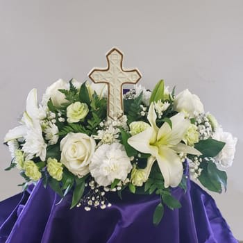 White floral arrangement with a cross centerpiece on purple cloth