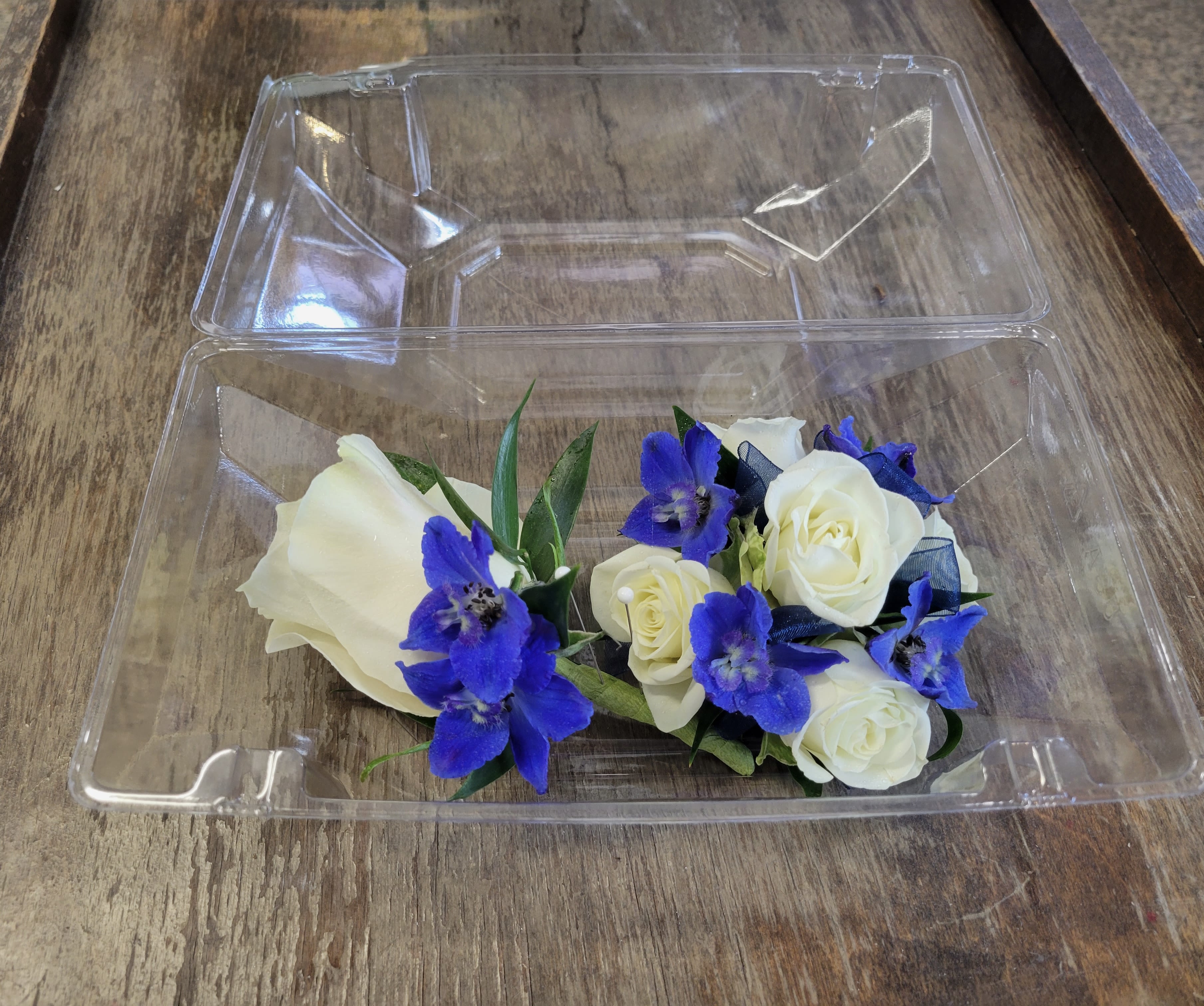 White roses and blue flowers in a clear plastic box