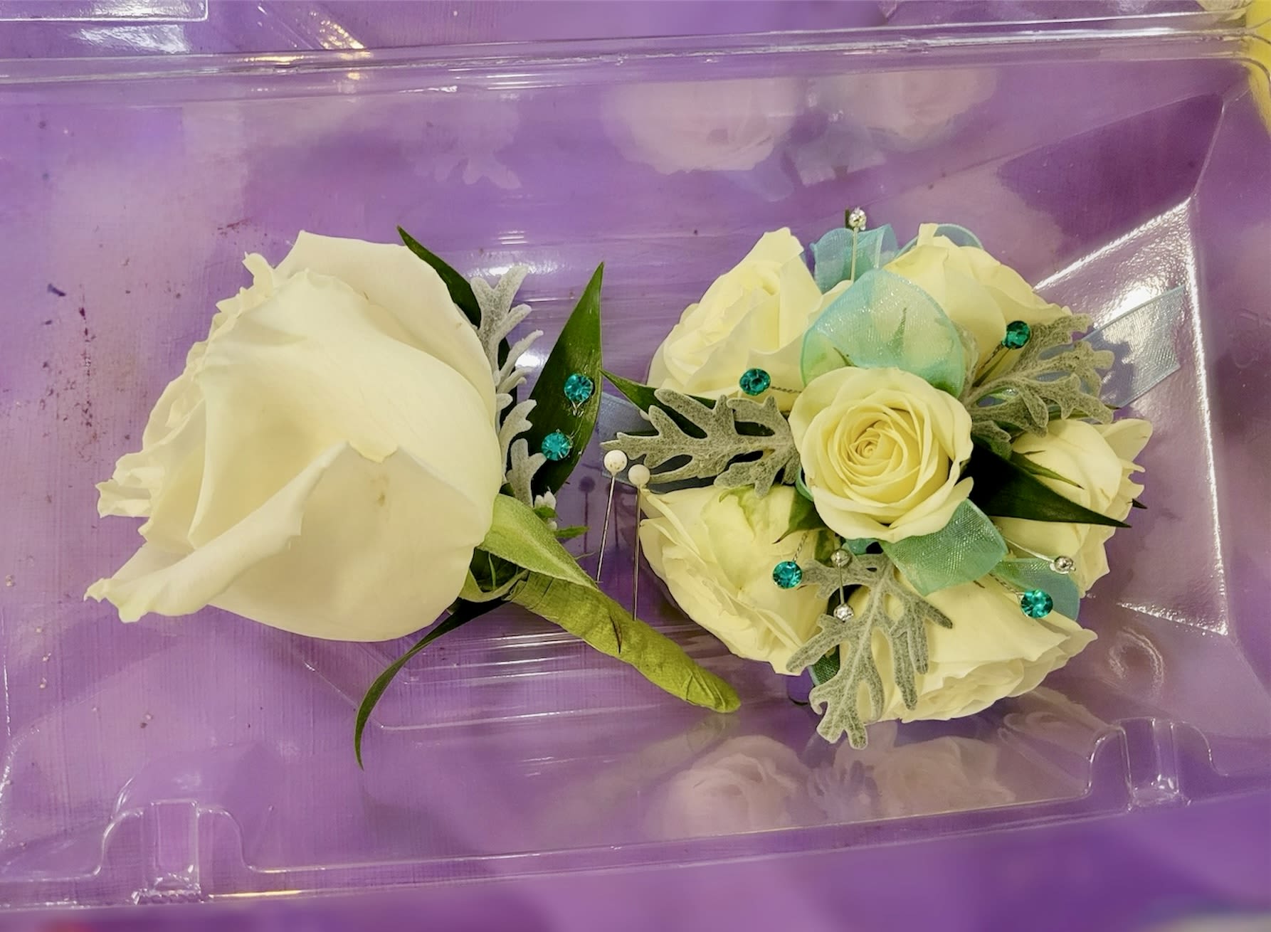 Two cream rose corsages in a purple plastic box