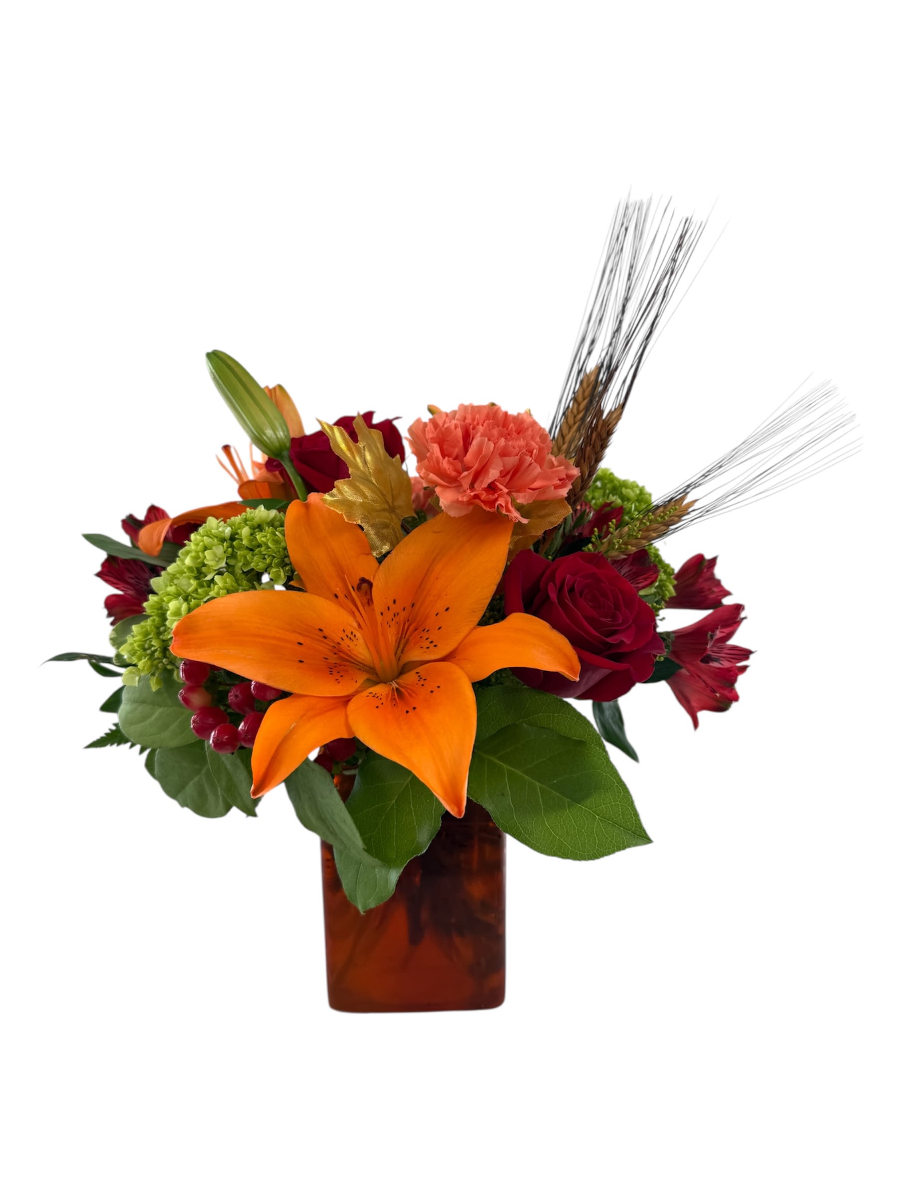 Whispers of Autumn - A vibrant and warm arrangement that captures the feeling of autumn. It features a stunning orange lily surrounded by red roses and alstromeria, green hydrangea and orange carnations designed in a colored rectangular glass vase.