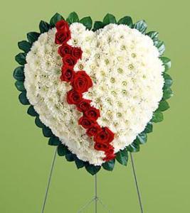 Heart-shaped floral tribute with white flowers and a red rose stripe on an easel