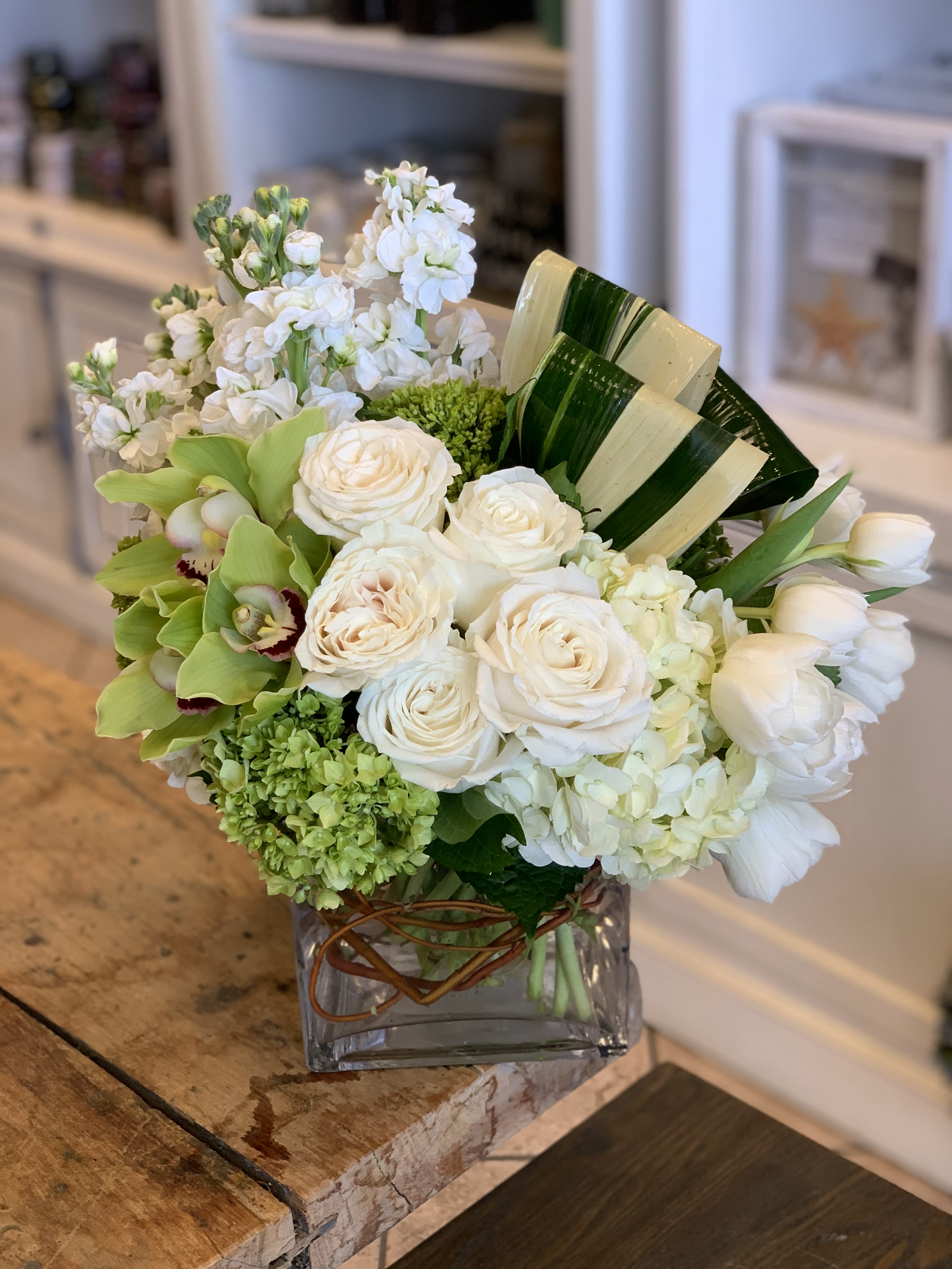 White roses and green orchids arranged in a square glass vase