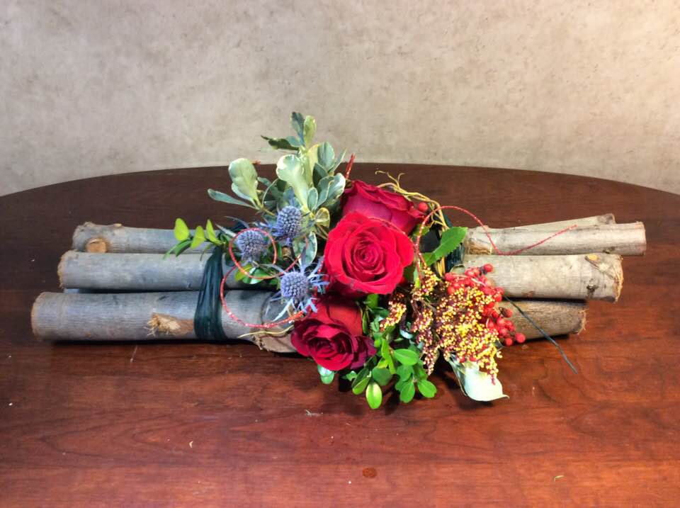 Red roses arranged with berries and greenery on bundled branches