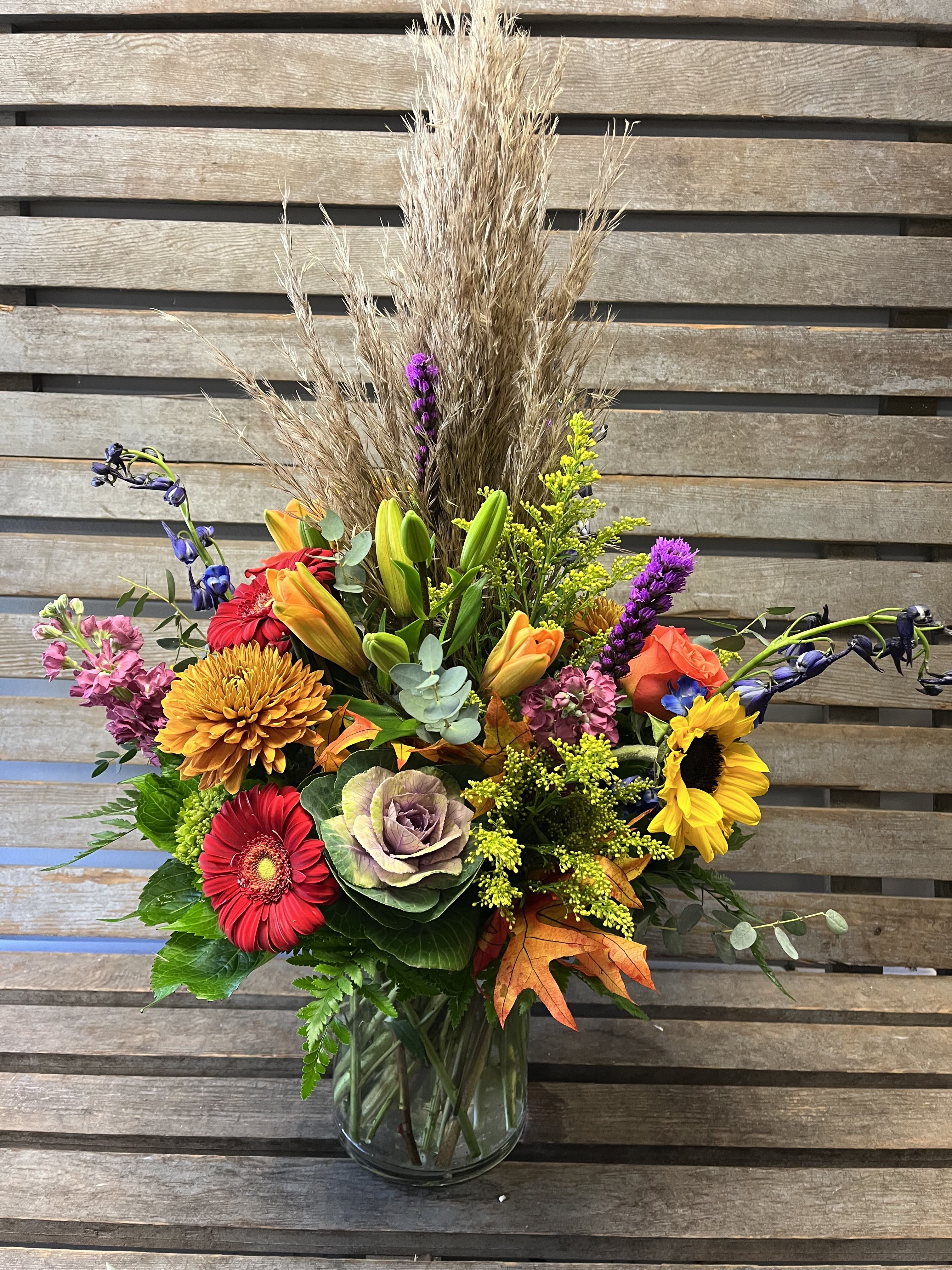 Mixed autumn bouquet in a clear glass vase with sunflowers, lilies, and chrysanthemums