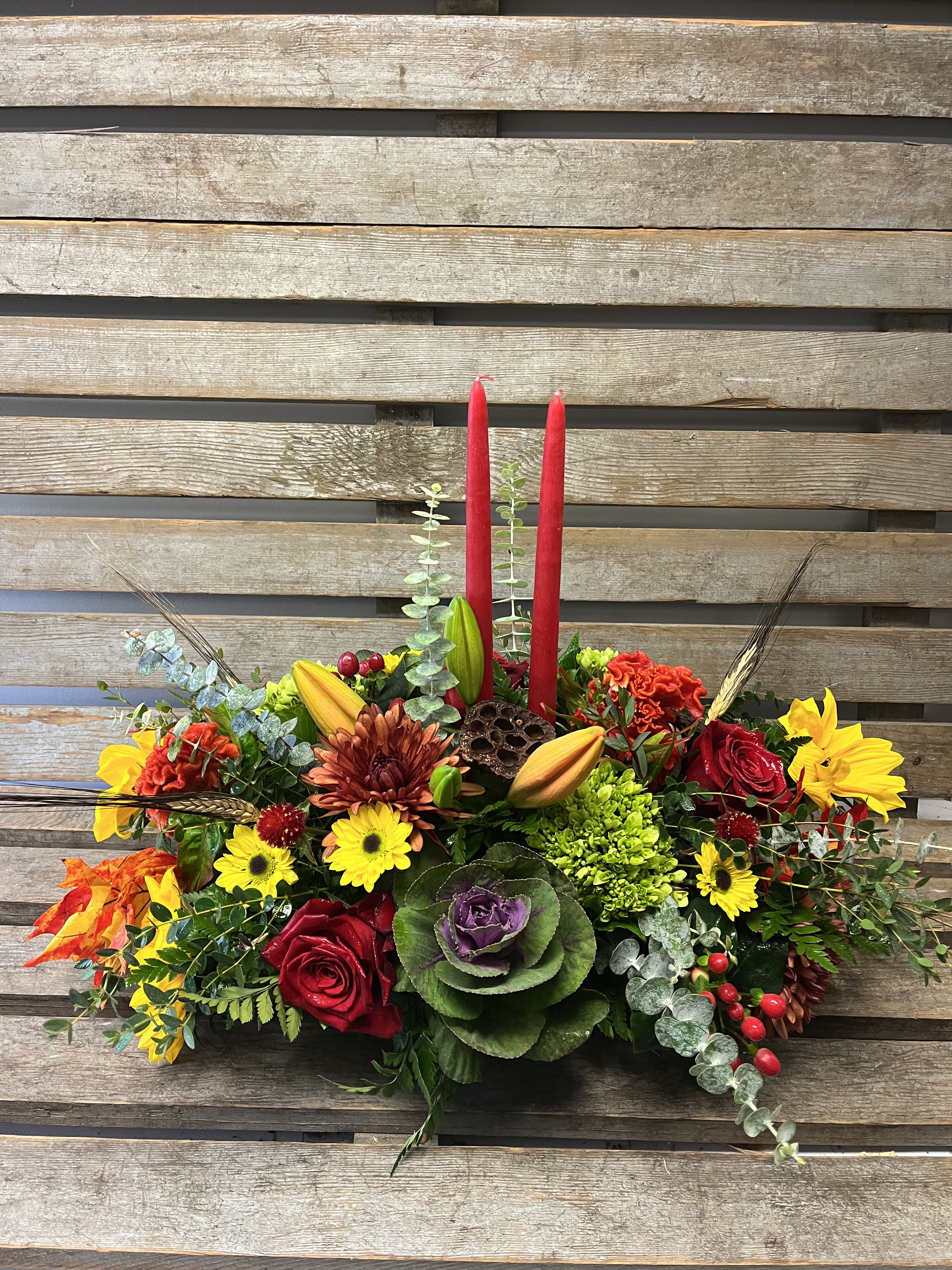 Colorful floral centerpiece with red candles and mixed blooms on a wooden backdrop