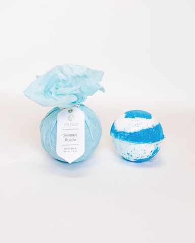 Blue bath bomb wrapped in tissue paper beside a striped bath bomb
