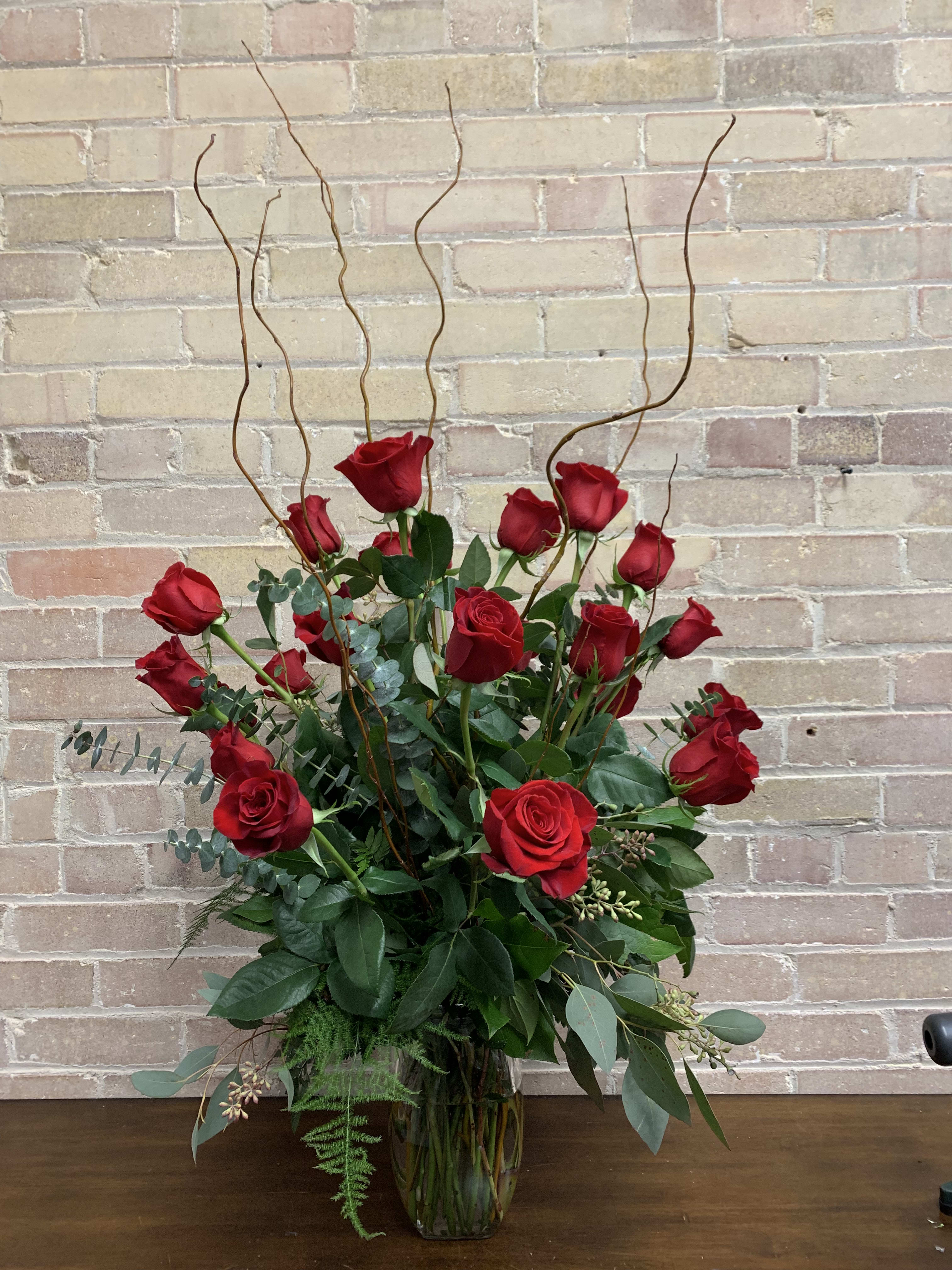Tall bouquet of red roses in a glass vase with curly branches