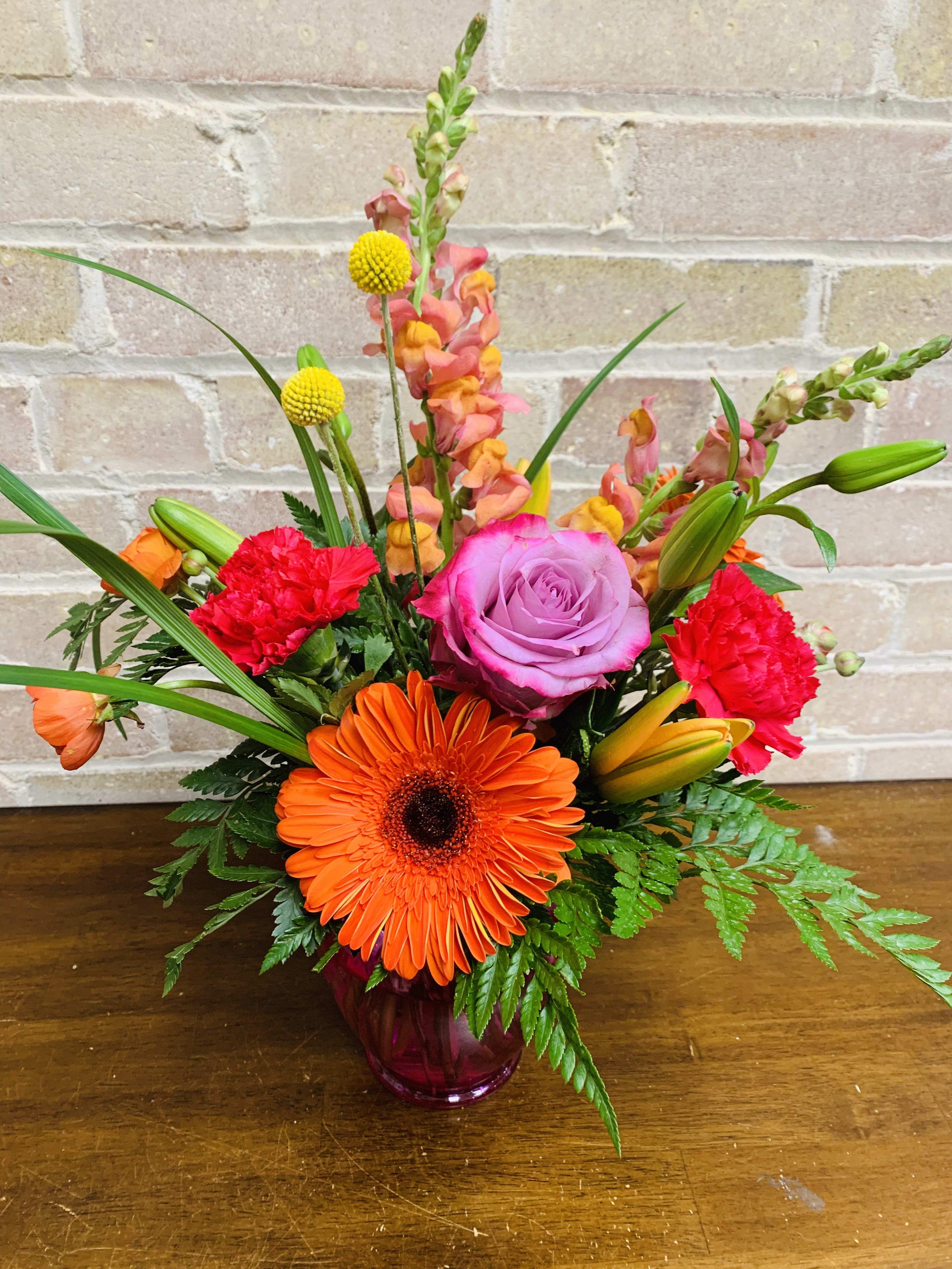 Bright mixed bouquet in a purple glass vase with orange, pink, and red blooms