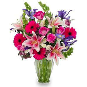 Mixed bouquet of pink lilies, roses, and gerbera daisies in a glass vase