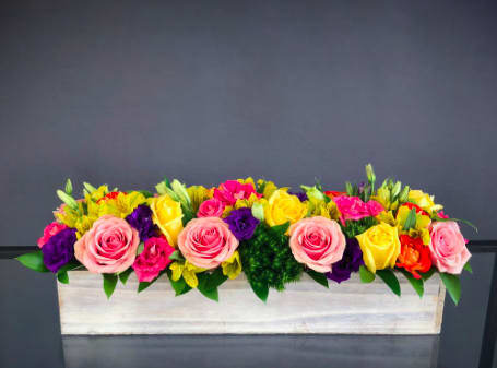 Long rectangular flower arrangement with pink, yellow, purple, and orange blooms in a white box