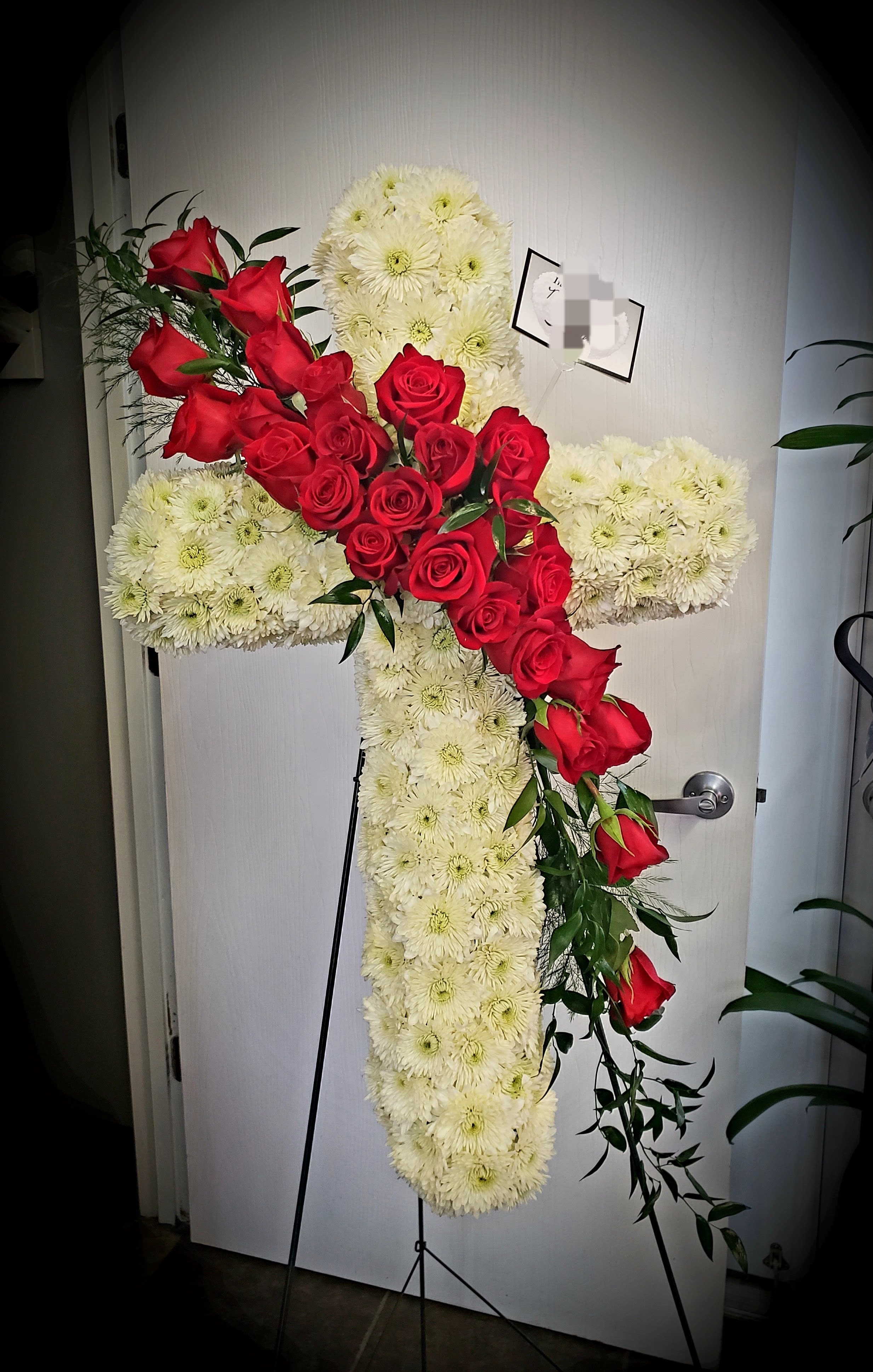 Faithful Cross of Splendor by The Potted Plant - A 30" cross covered in white cushion pompons and a spray of red roses create this faithful cross of spendor. Roses can be done in Red, Lavender, Yellow, Pink and Orange. 