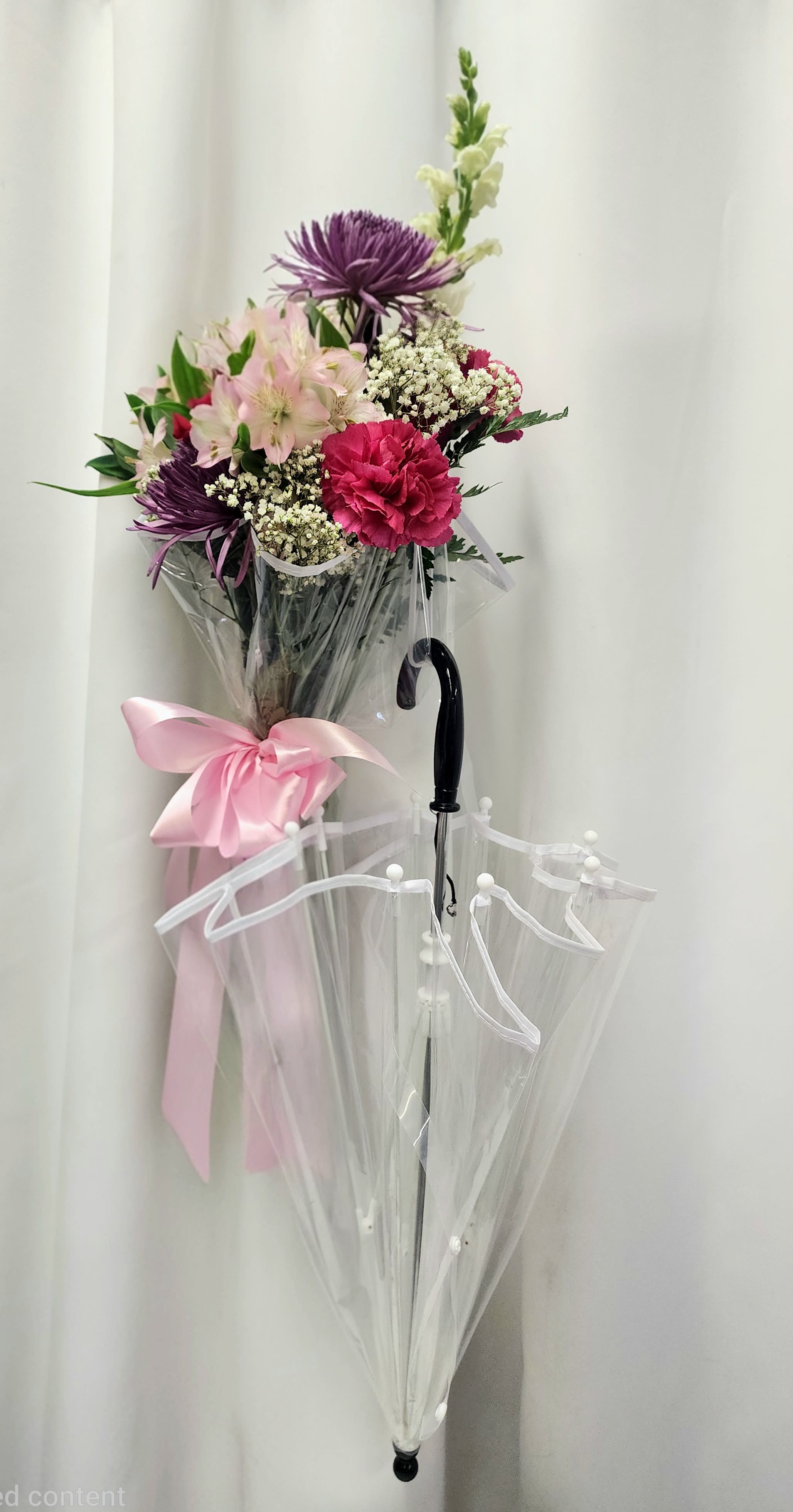 Rain or Shine - Brighten any day, come rain or shine, with this charming floral arrangement! A delightful selection of fresh blooms artfully arranged inside a functional clear umbrella, making it a multi-purpose gift that’s as practical as it is beautiful. Whether you’re celebrating a special occasion or simply want to bring a smile, this arrangement offers both charm and utility. If you have a preferred color palette, just add a note to your florist at checkout—otherwise, let our designers surprise you with their creative touch! 