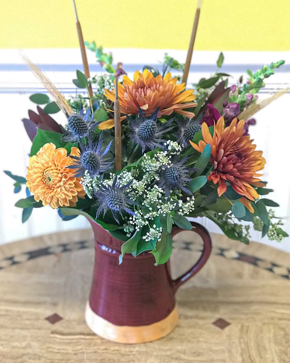 Mixed bouquet in a burgundy pitcher vase with orange and blue flowers