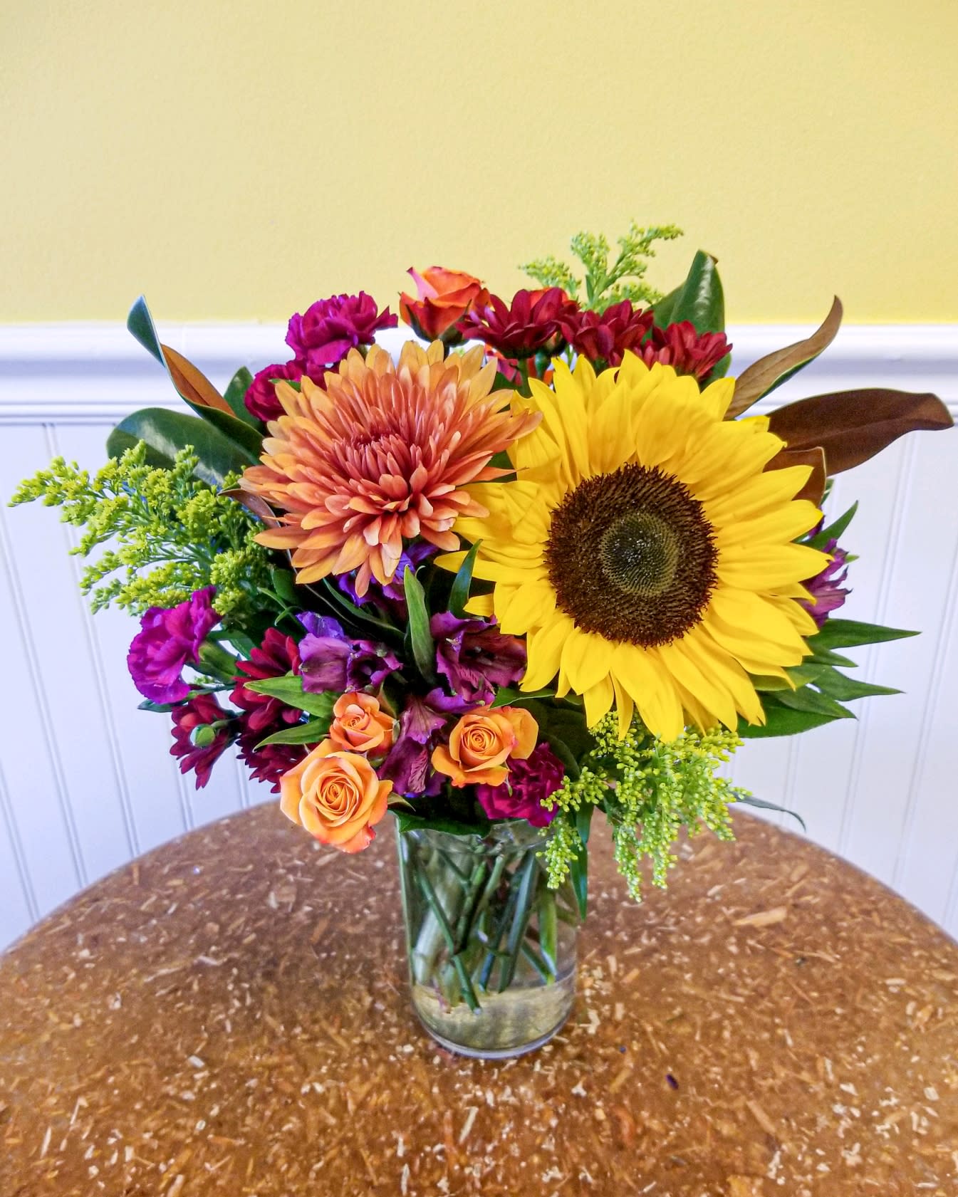 Mixed bouquet in a clear glass vase with a large sunflower and orange blooms