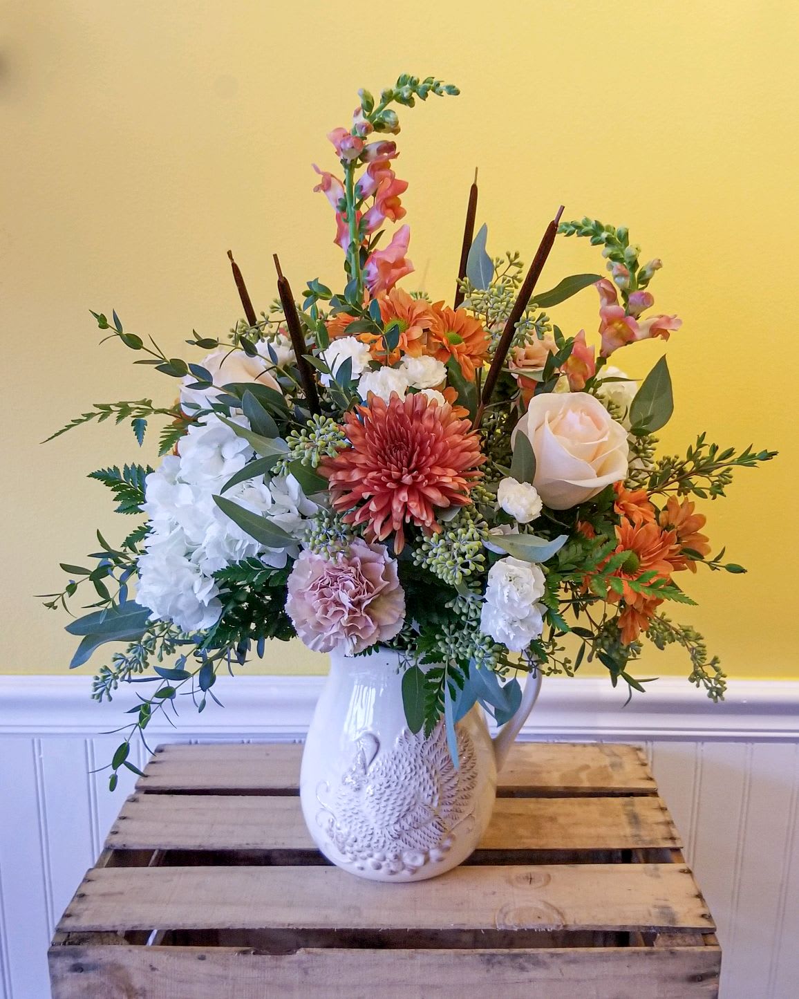 Mixed floral arrangement in a white ceramic pitcher vase