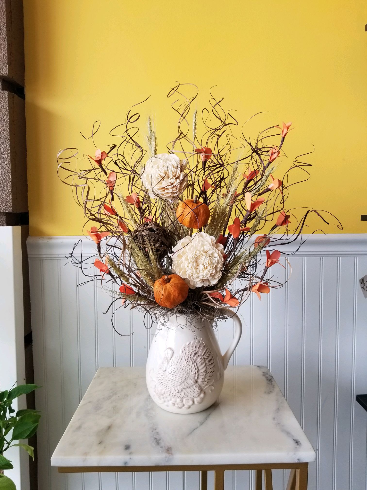Autumn floral arrangement in a white pitcher vase with cream blooms and orange accents