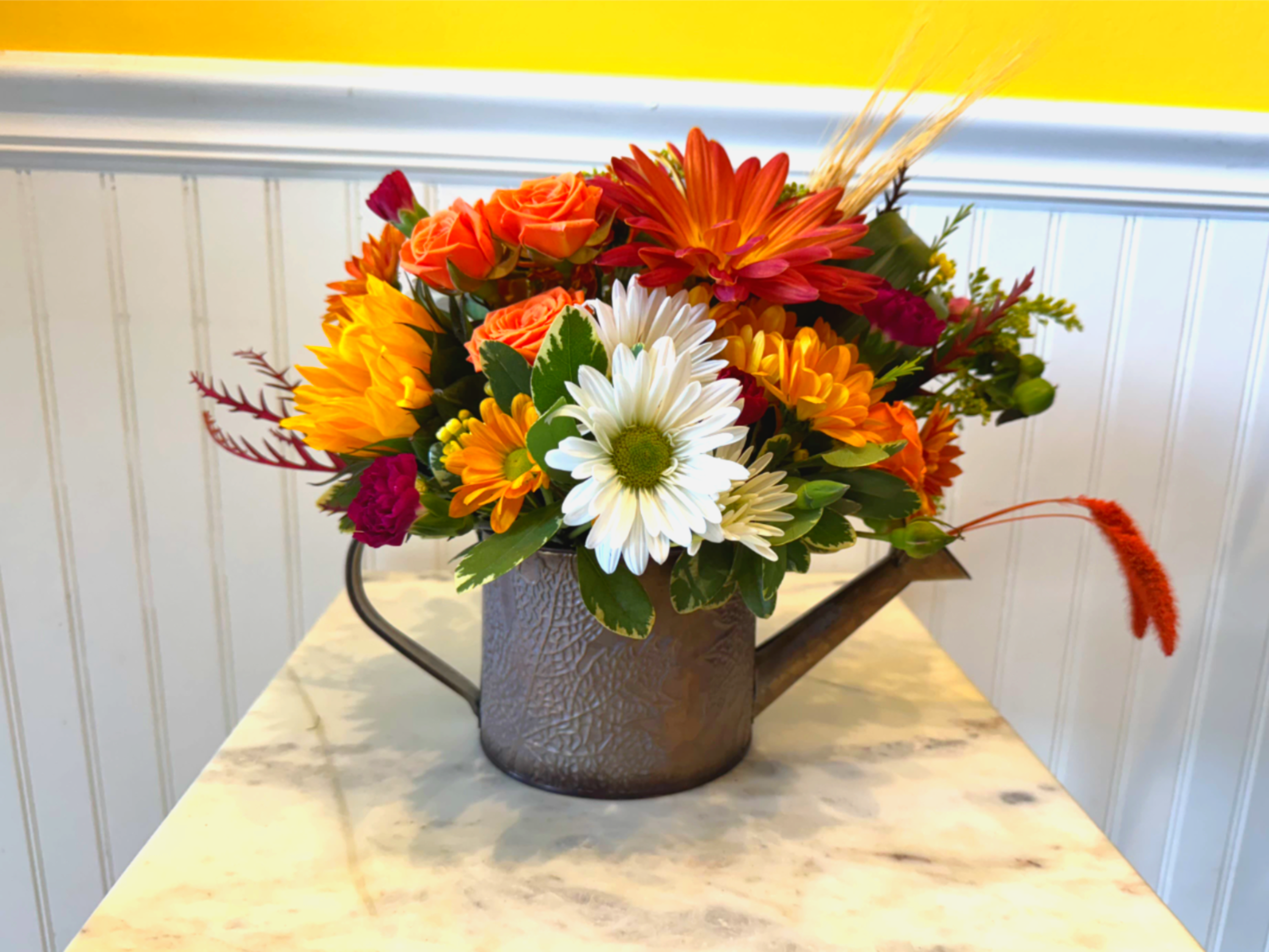 Mixed orange, white, and yellow flowers arranged in a metal watering can