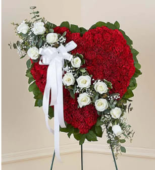 Heart-shaped red floral standing spray with white roses and a white ribbon bow on an easel.