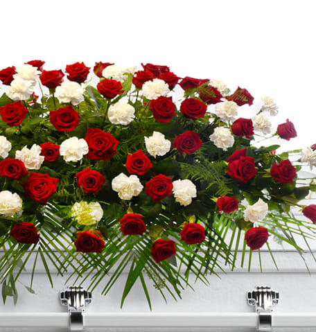 Red roses and white carnations arranged in a casket spray on a white casket