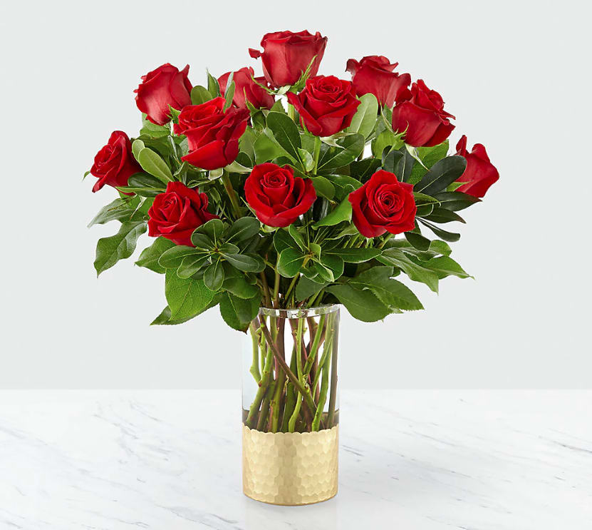 Red roses arranged in a clear glass vase with green foliage.