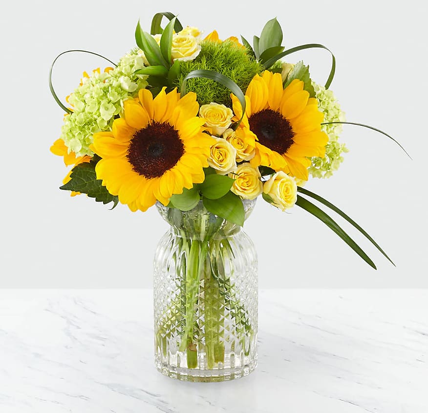 Sunflower and yellow rose arrangement in a clear glass vase