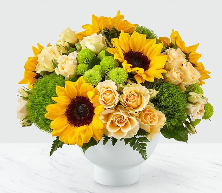 Truly Radiant™ Bouquet - From the bold beauty of bright sunflowers to the sweet delight of peach spray roses, our Truly Radiant Bouquet captures every expression of true happiness. Complete with bursts of green trick dianthus and button pompons, this arrangement is set in a modern white ceramic vase to accent any home. Gift this bouquet for a special birthday or simply just because, it will surely brighten their day! 