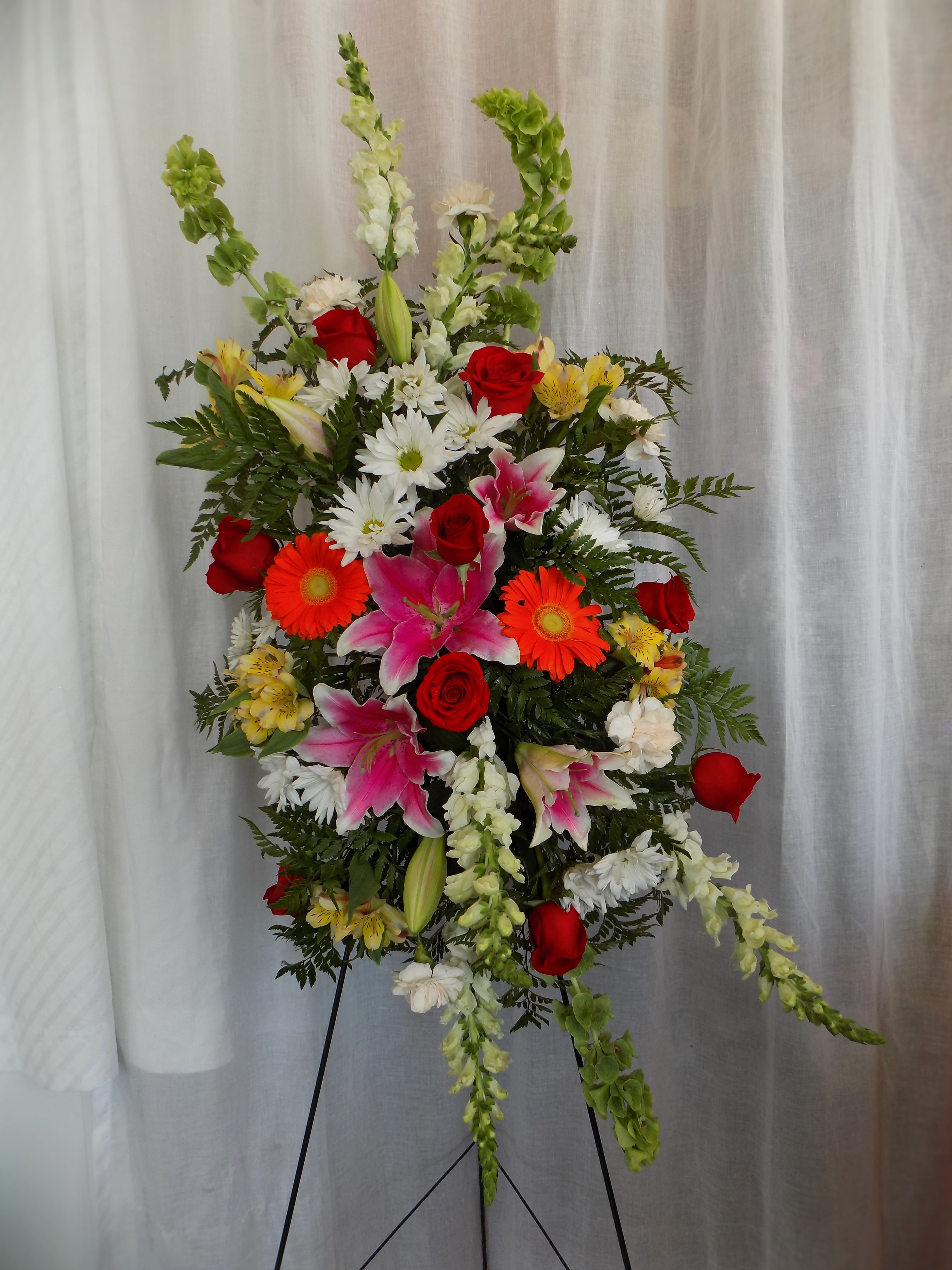 Tall standing floral spray with red roses, pink lilies, and white daisies