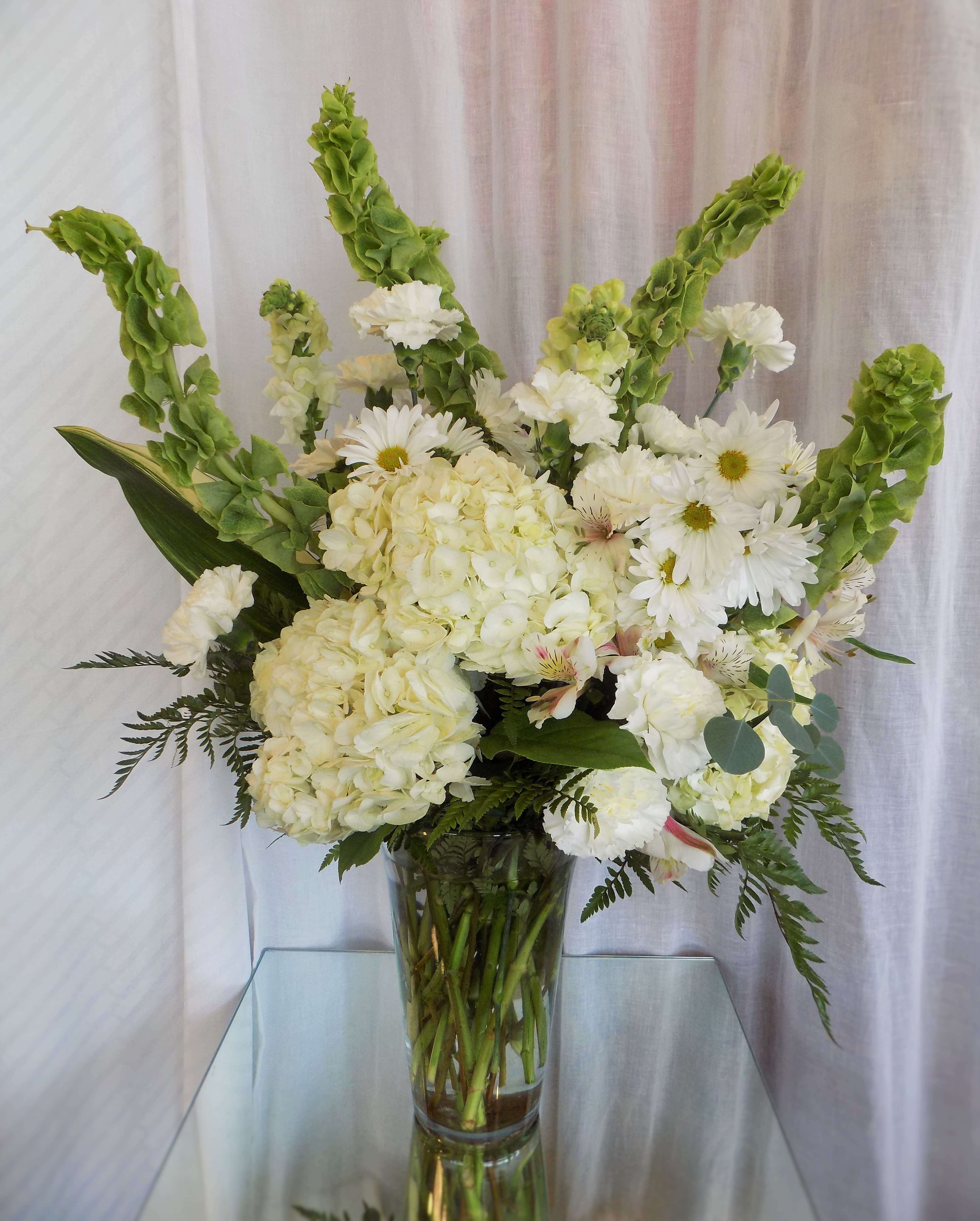 White floral arrangement in a clear glass vase with tall green spikes